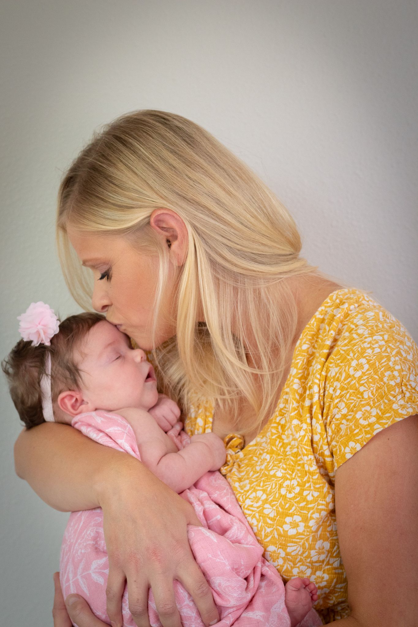 Tender moment between parent and baby in pink dress against neutral background.