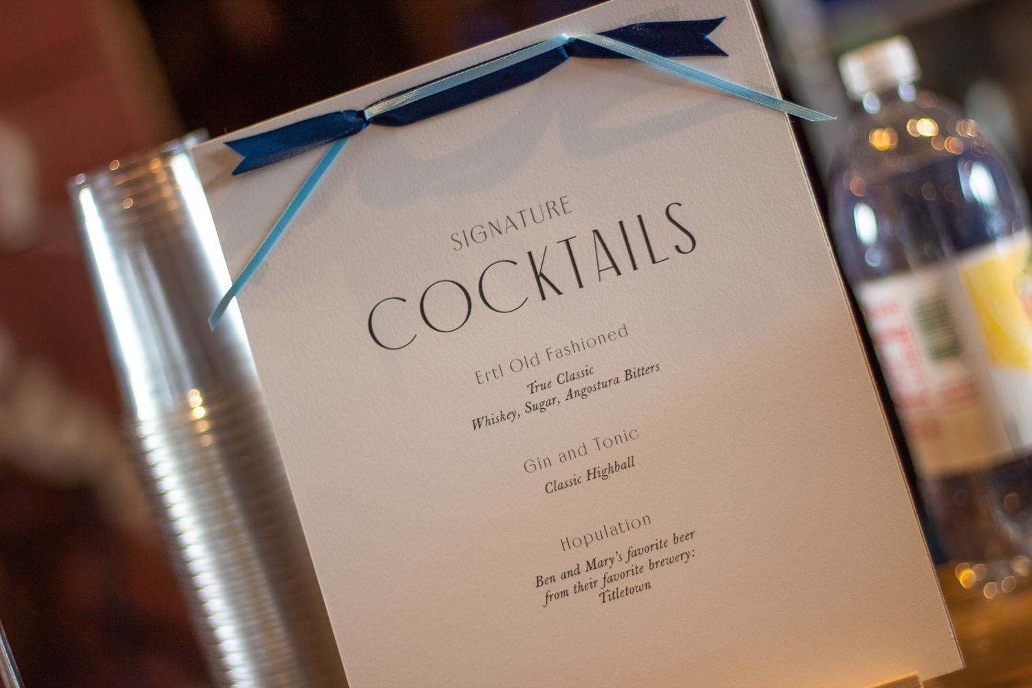 A cocktail menu card with a blue ribbon accent on display at an event.