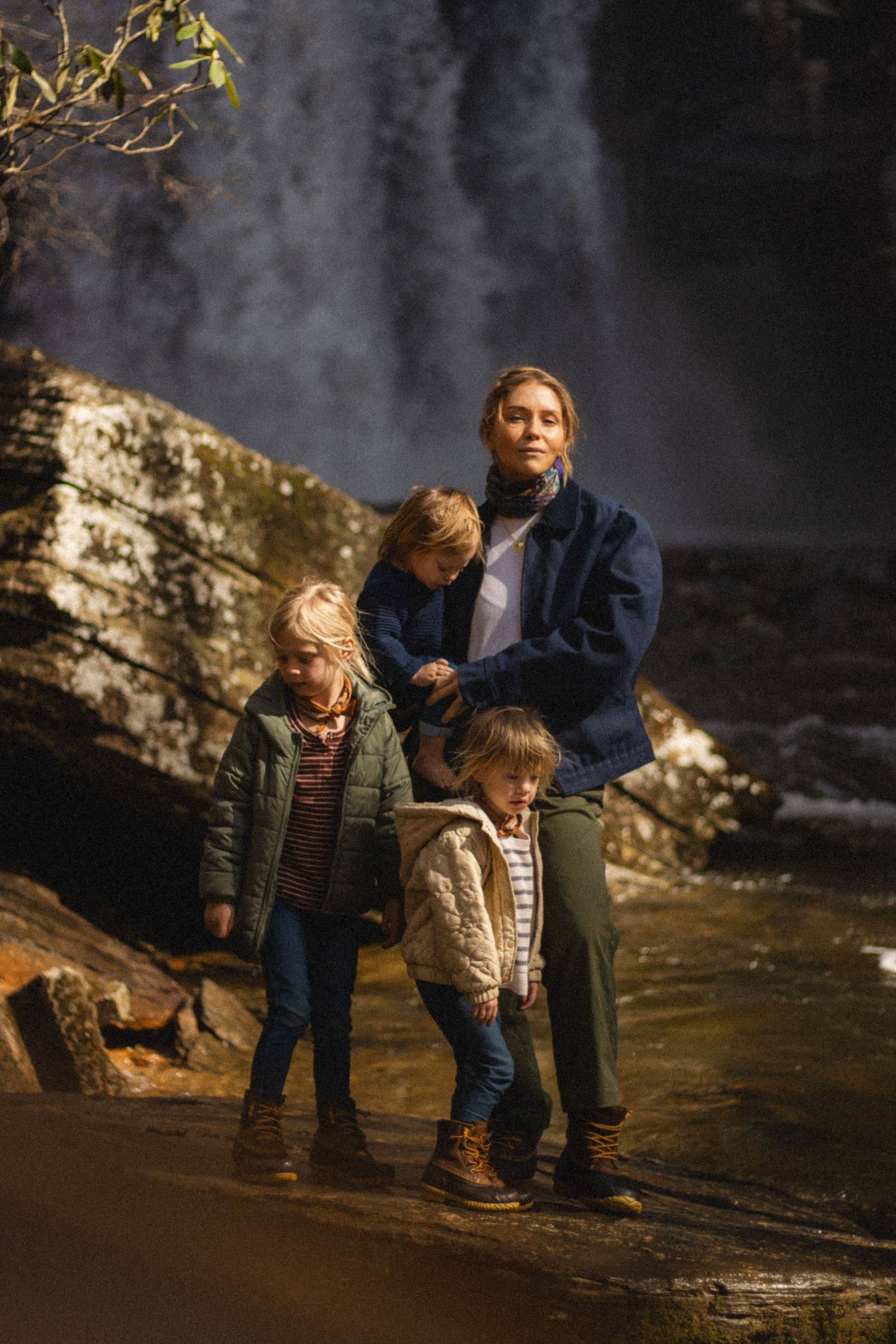 Parent and children pose together near dramatic waterfall against rocky backdrop.