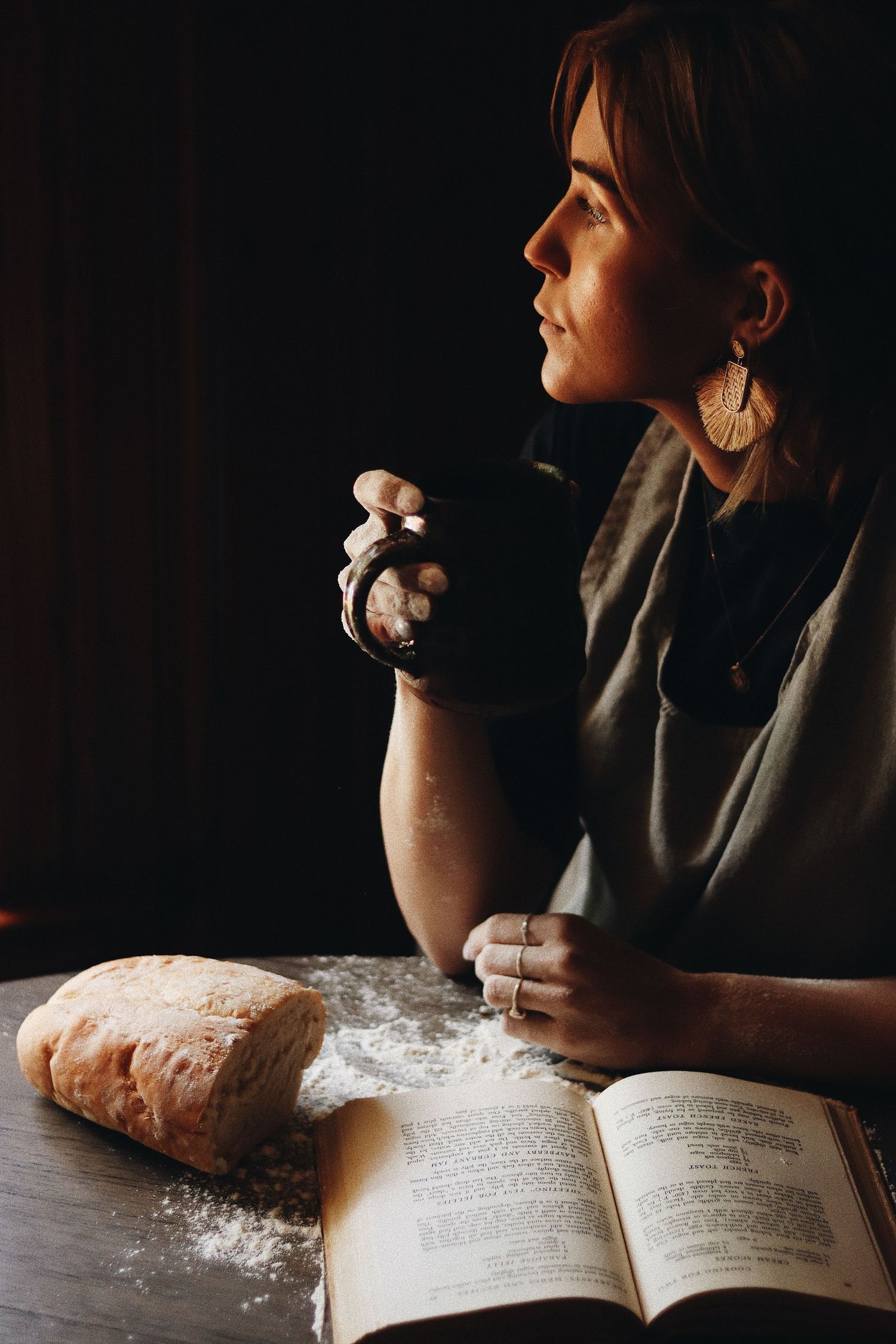 Person reading cookbook dusted with flour in moody lighting creating atmospheric baking scene.