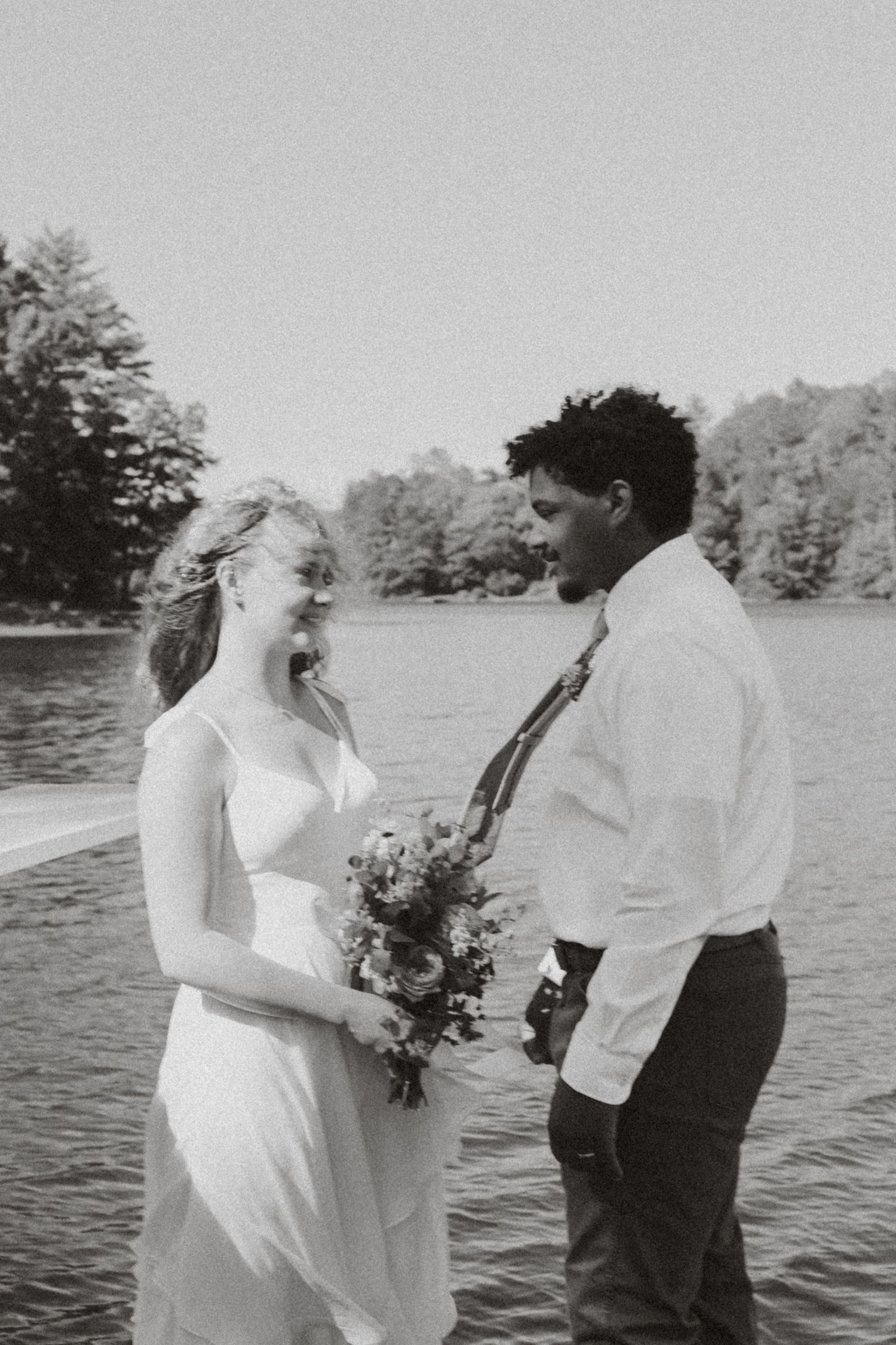 Couple sharing intimate moment by lake with bouquet of wildflowers.