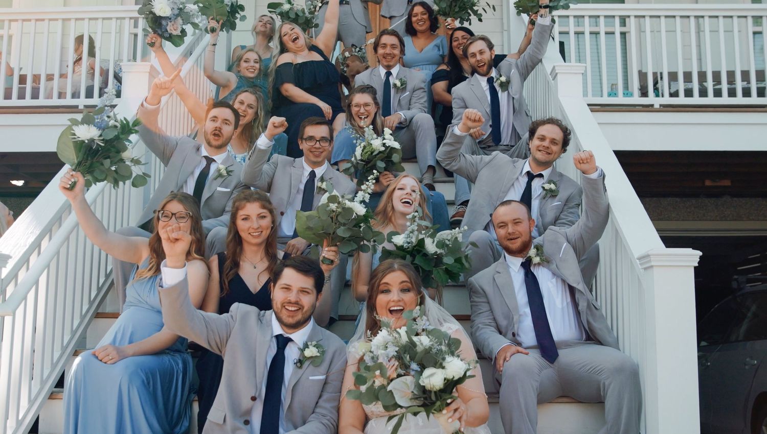 Panoramic wedding party photo with people celebrating on outdoor porch.