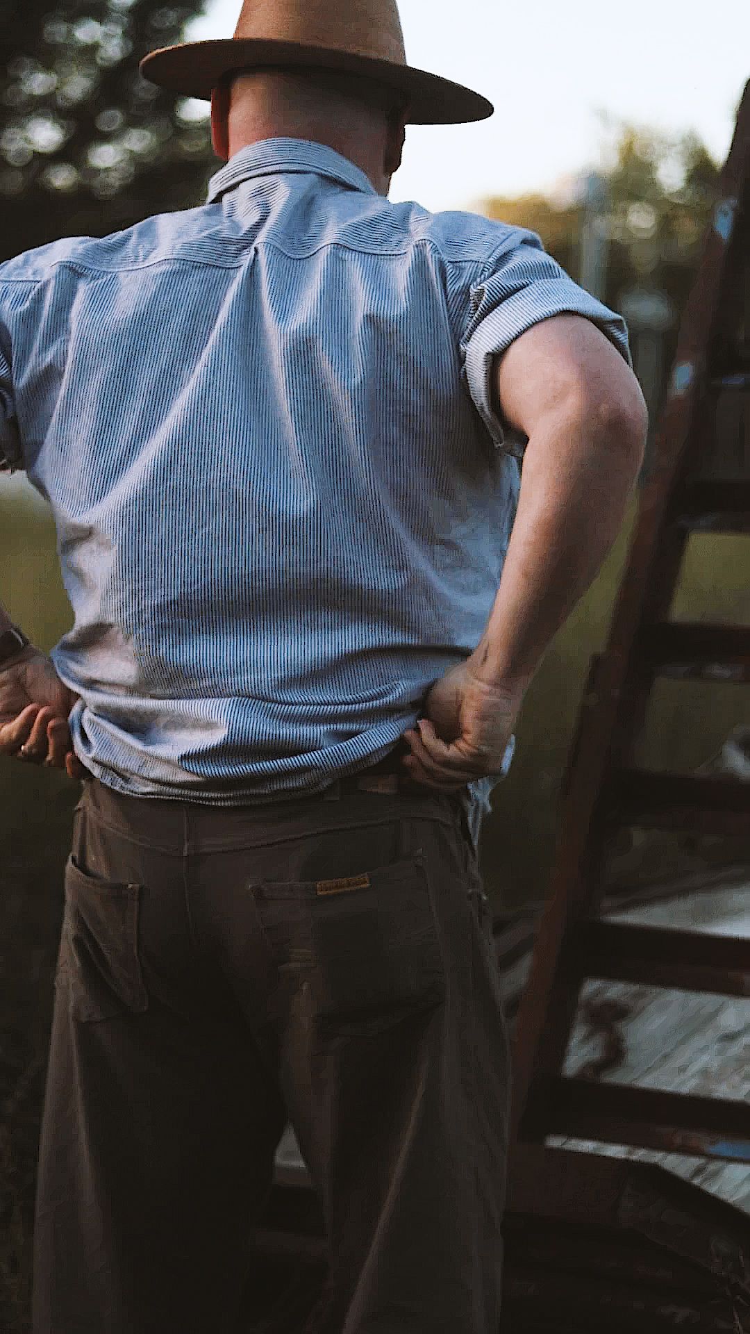 Person wearing light blue shirt and dark pants adjusts their clothing while standing in a casual pose.
