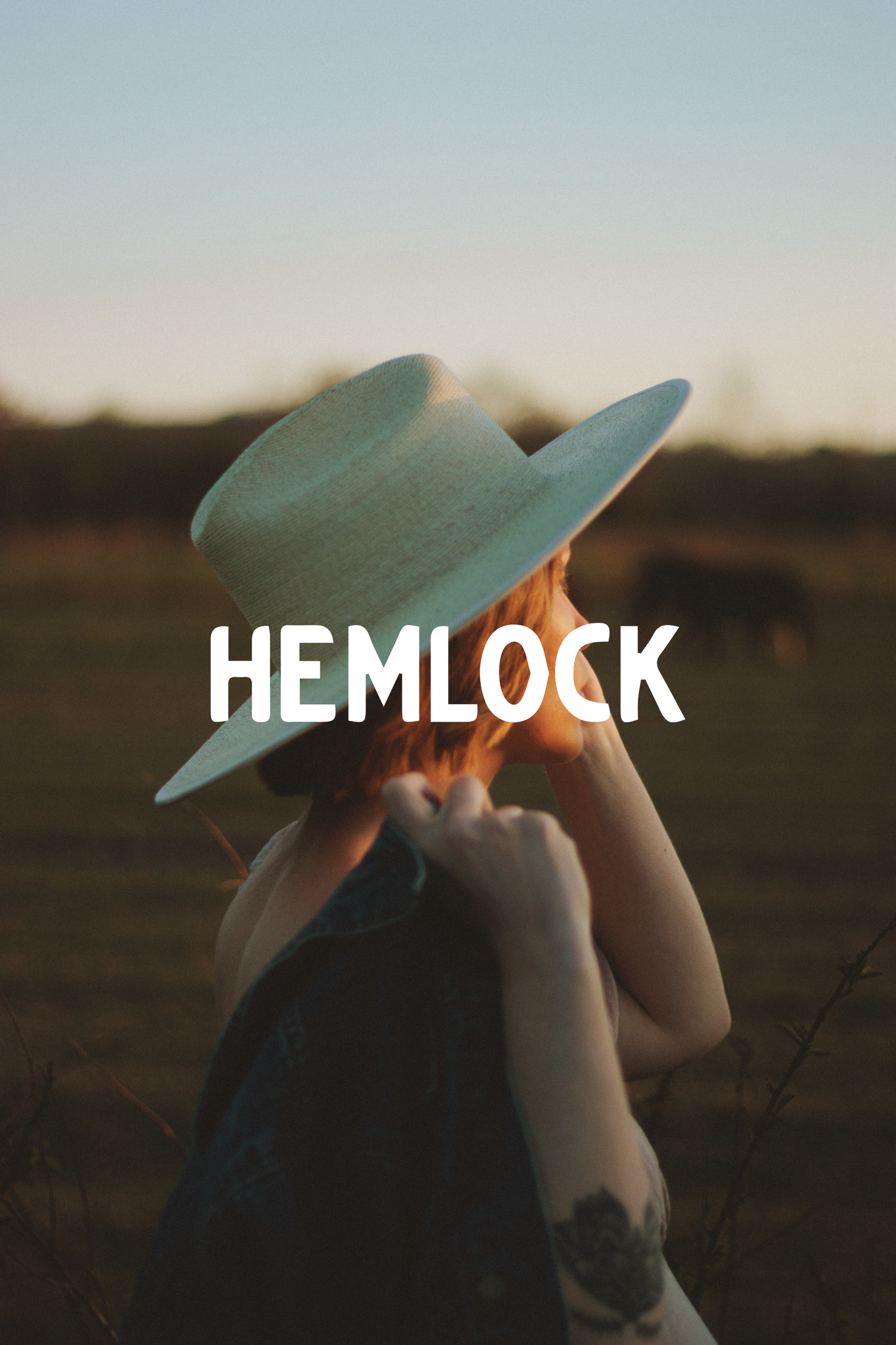 A dreamy sunset photo of a person wearing a wide-brimmed hat with the word HEMLOCK overlaid in white text.