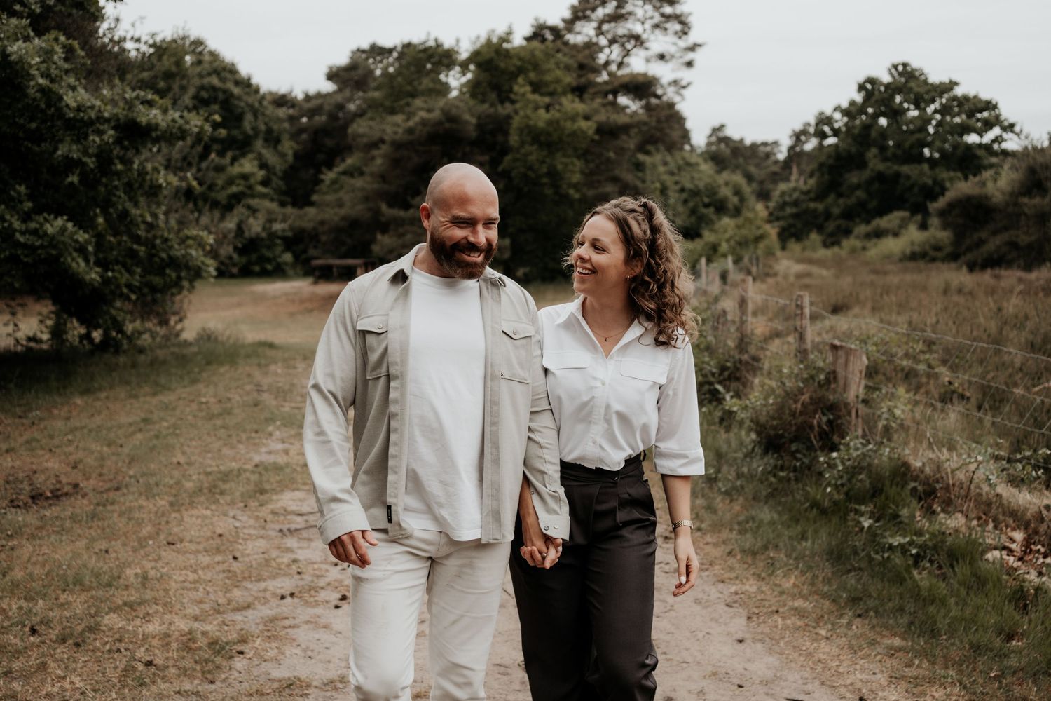 coupleshoot op een mooie buitenlocatie, vriend en vriendin houden hand vast en kijken ernaar