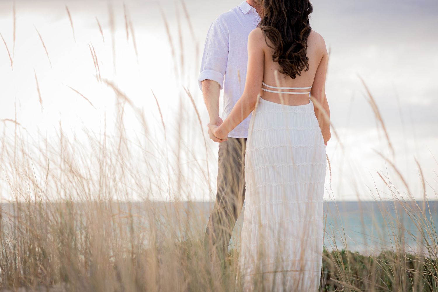 Engaged couple smiling and holding hands during their engagement photo session at leighton beach watching sunset