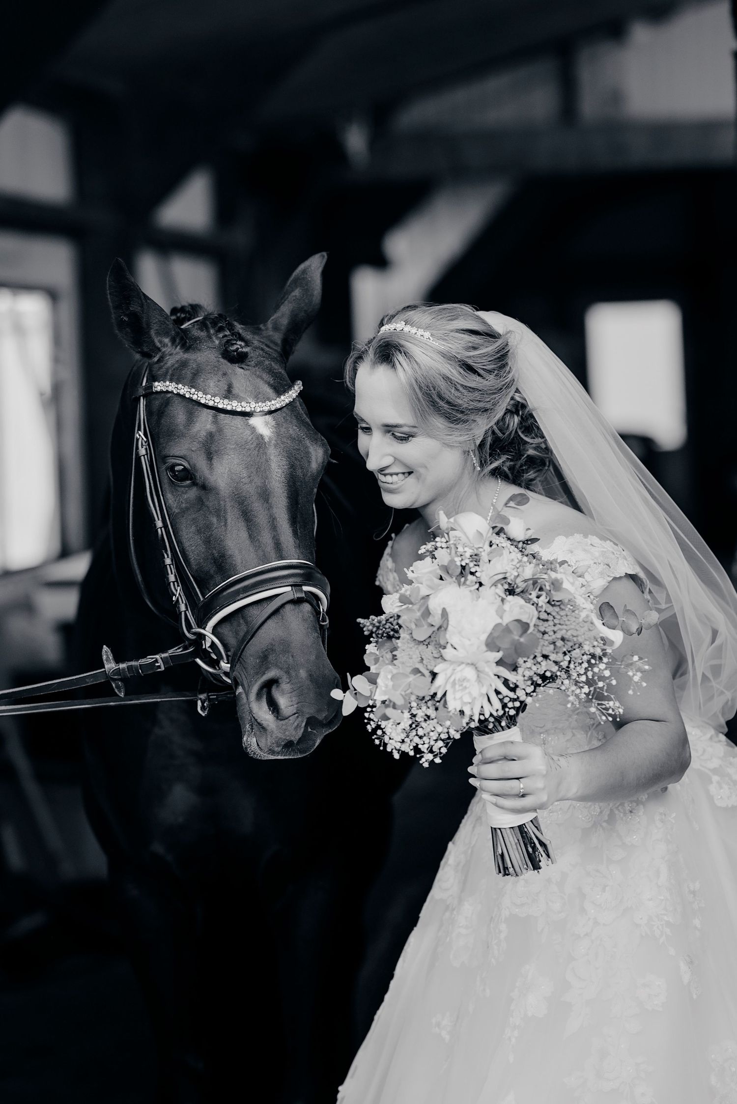 A tender moment between a bride and a horse in black and white, featuring a bouquet and a delicate veil.