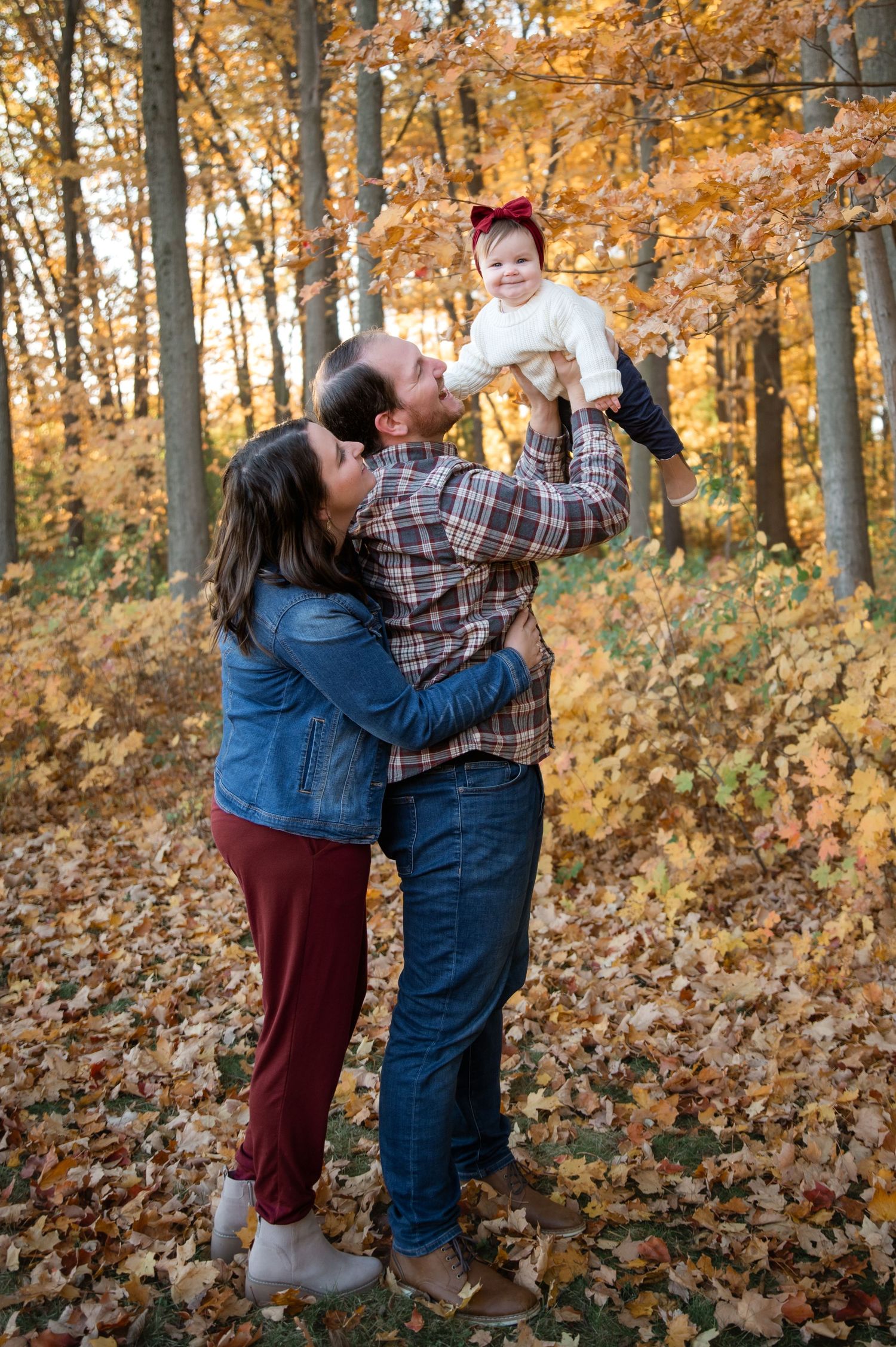 Two people in casual attire play with a small child among vibrant autumn foliage in a forest setting.