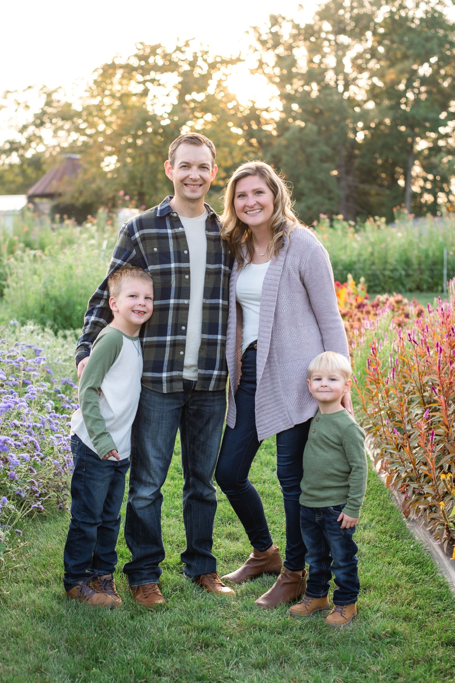 A family stands together outdoors in a garden with colorful flowers and greenery at sunset.