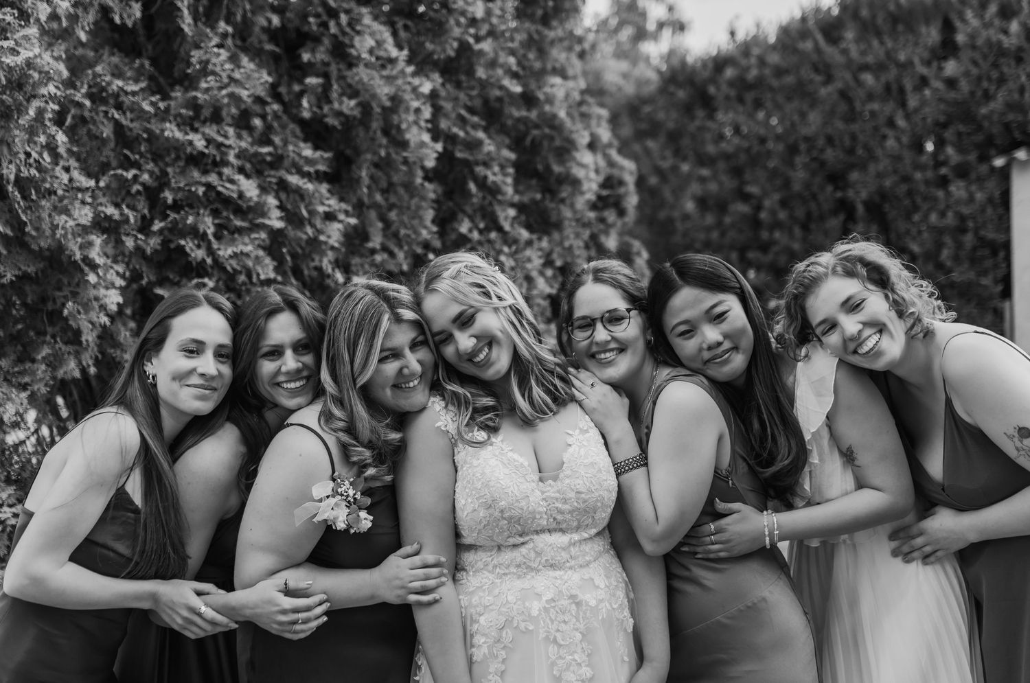 Black and white candid photo of bridesmaids laughing together in a garden setting.