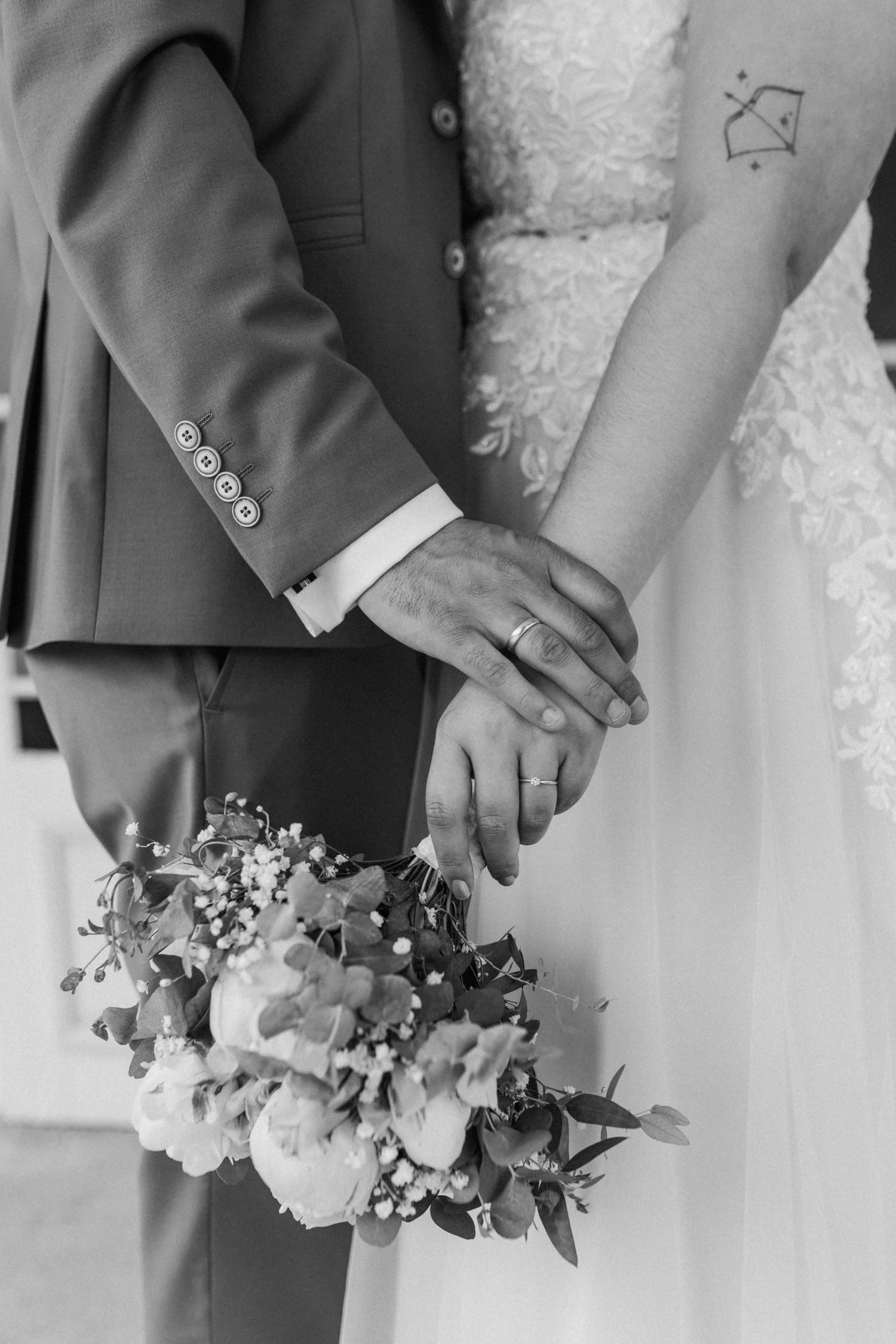 Close-up of couple's hands holding bouquet showing wedding rings and formal attire.