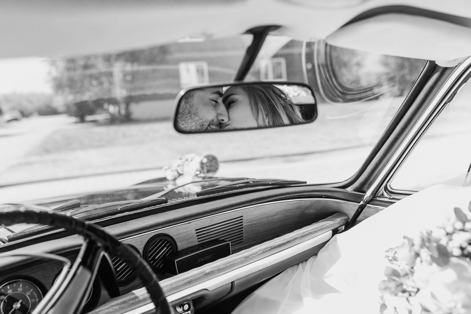 Black and white view of bride's reflection in classic car rearview mirror.
