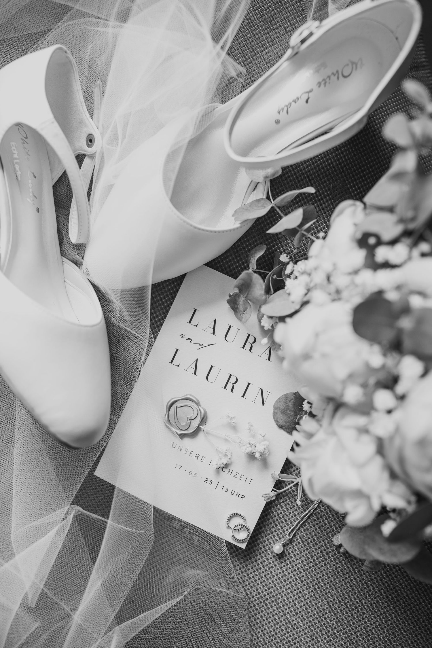 White wedding shoes and invitation card arrangement with floral details.