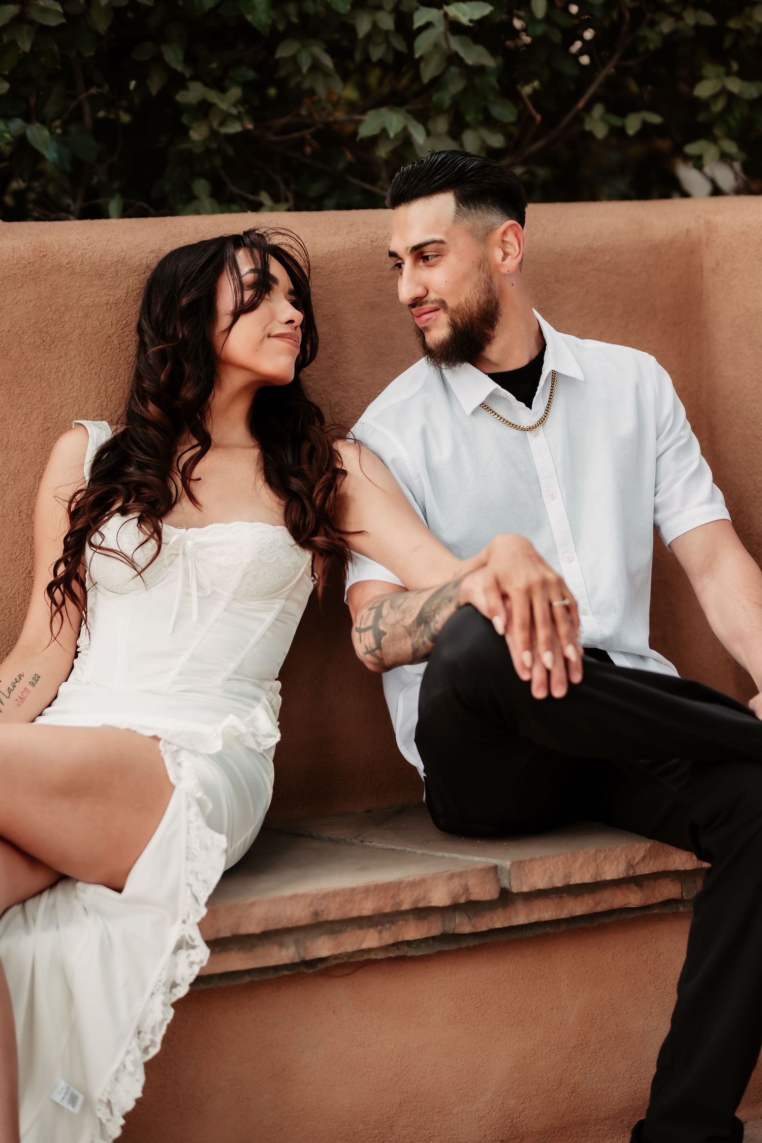 Intimate portrait of couple relaxing on adobe bench in matching white outfits.