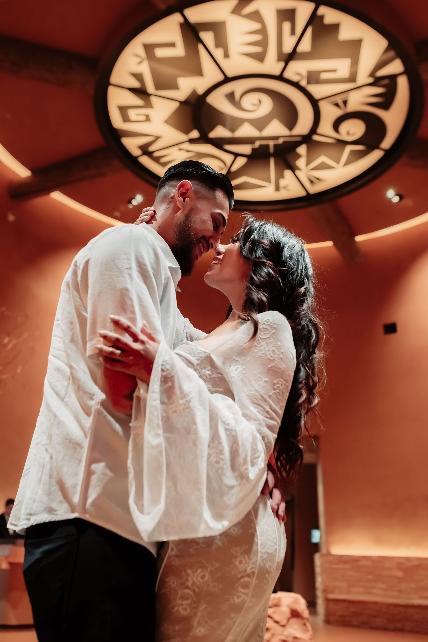 A couple dancing in a ballroom under a decorative ceiling medallion.