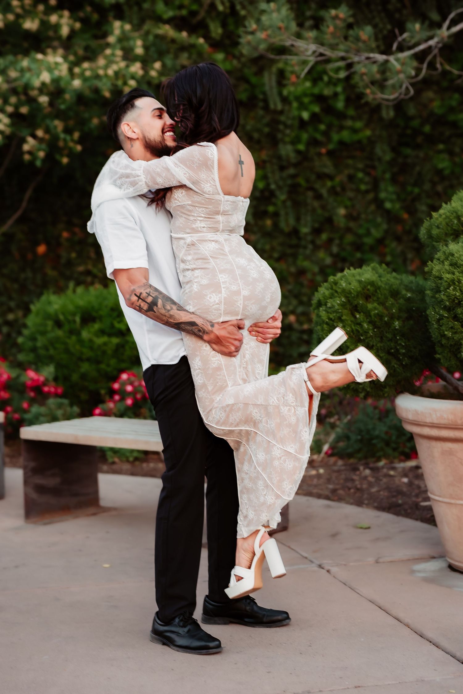 Playful outdoor portrait of couple in formal attire against garden backdrop.