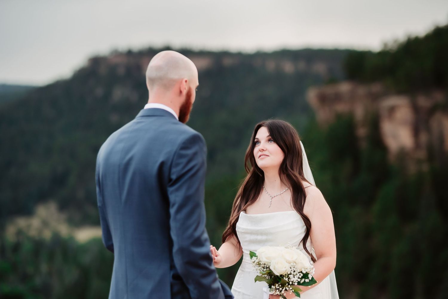 A wedding couple shares an intimate moment on a scenic mountain cliff edge.