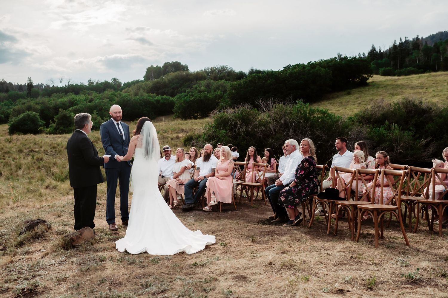 An outdoor wedding ceremony with rustic wooden chairs set against rolling hills and forest.