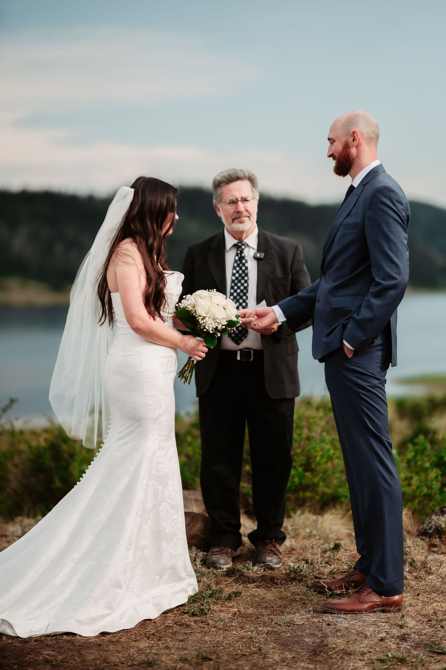 Intimate outdoor wedding ceremony by a lake with white wedding dress and navy suit.