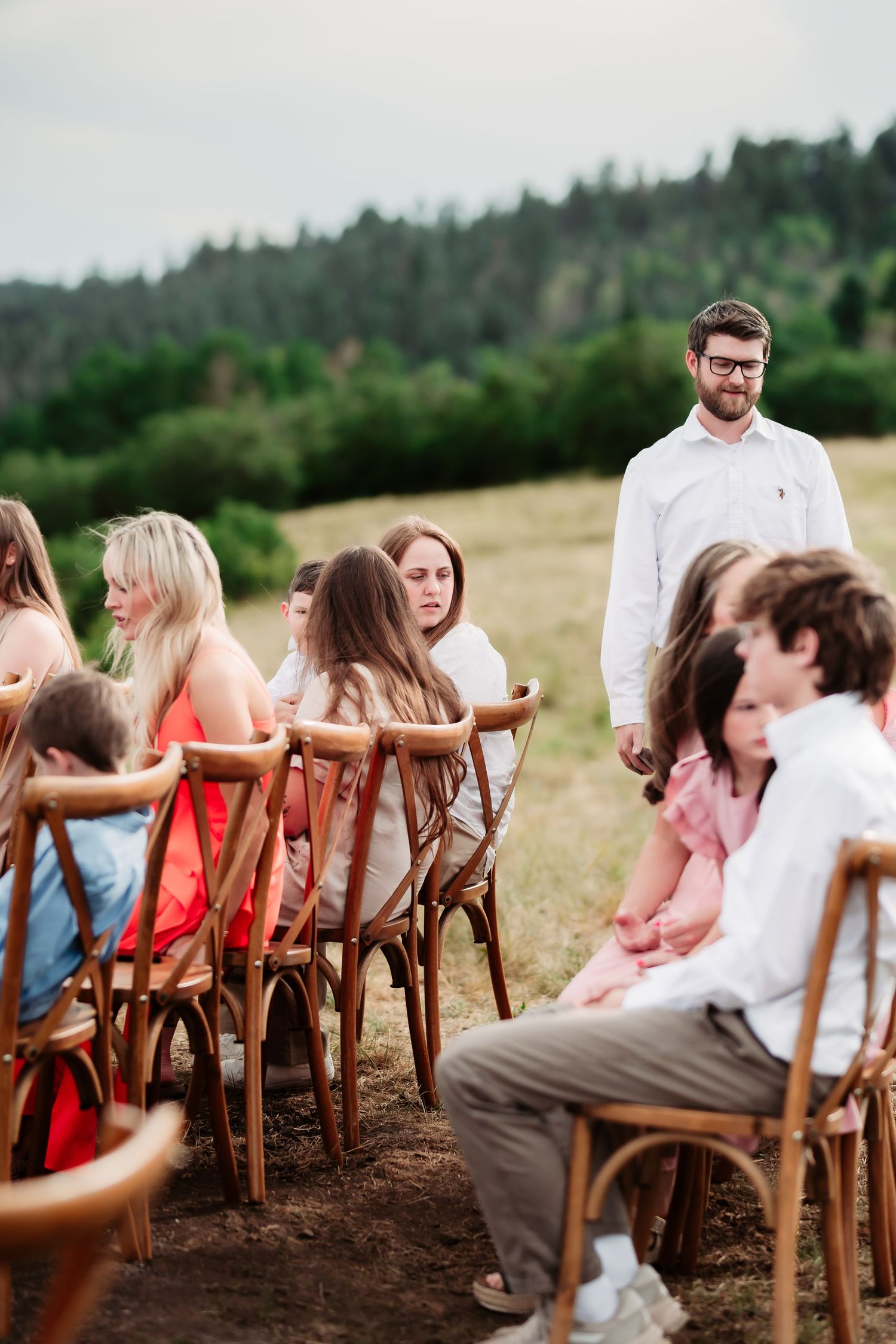 Wedding guests seated in wooden chairs at an outdoor ceremony with mountain views.
