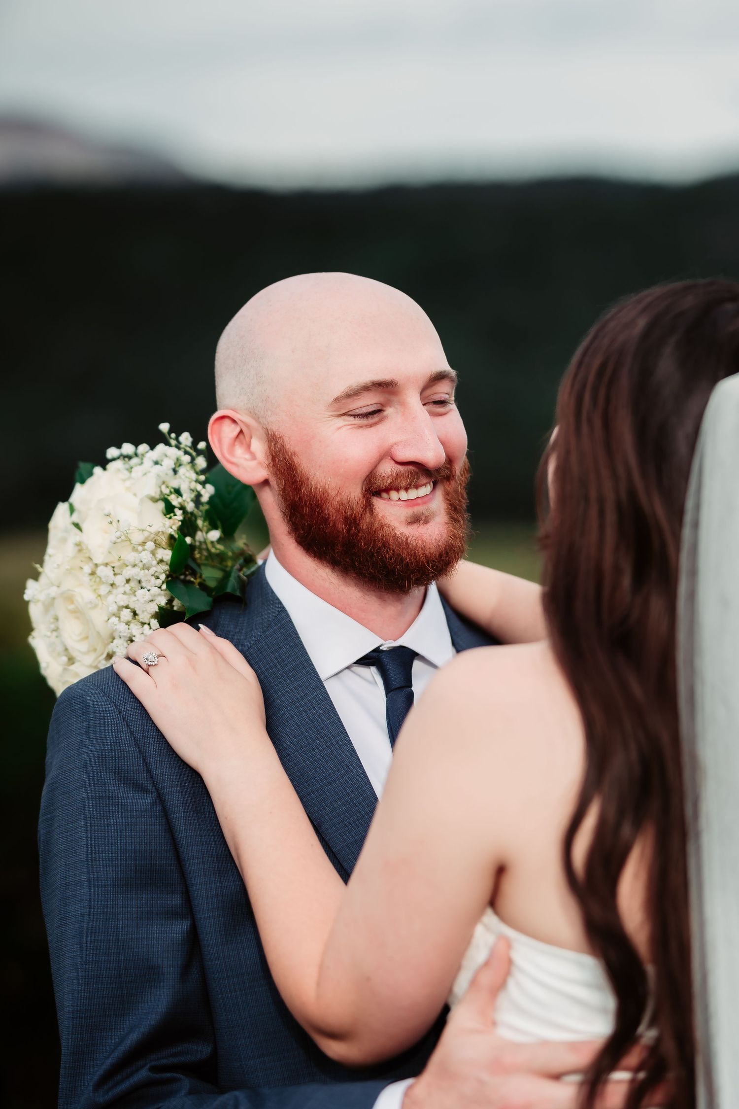 A tender moment between newlyweds with white flowers against a mountain backdrop.