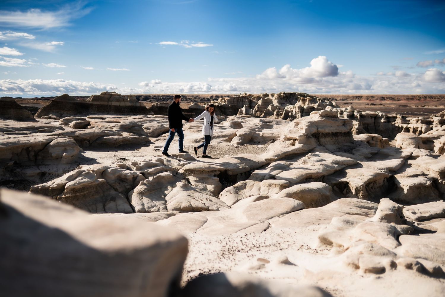 Two adventurers explore unique rock formations in a desert landscape under bright blue skies.