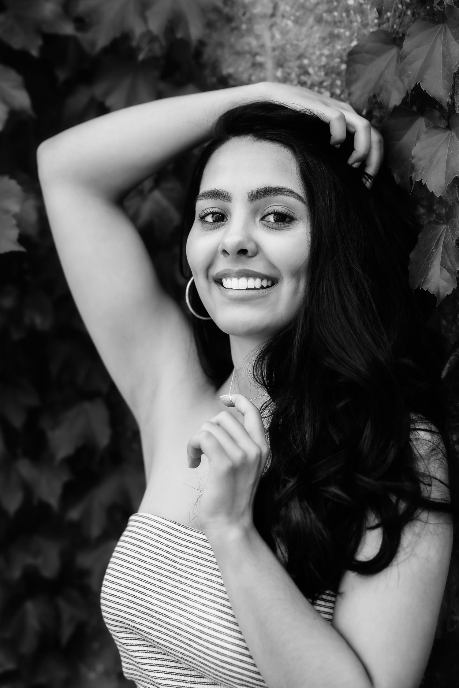 Black and white closeup portrait with hoop earrings against ivy backdrop.