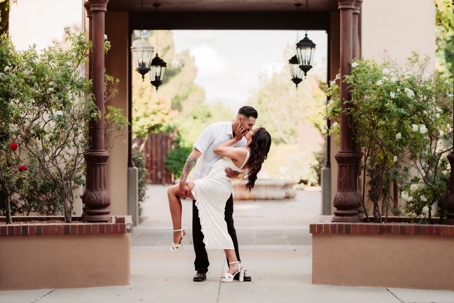 Couple sharing dramatic dip pose under rustic archway during photoshoot.