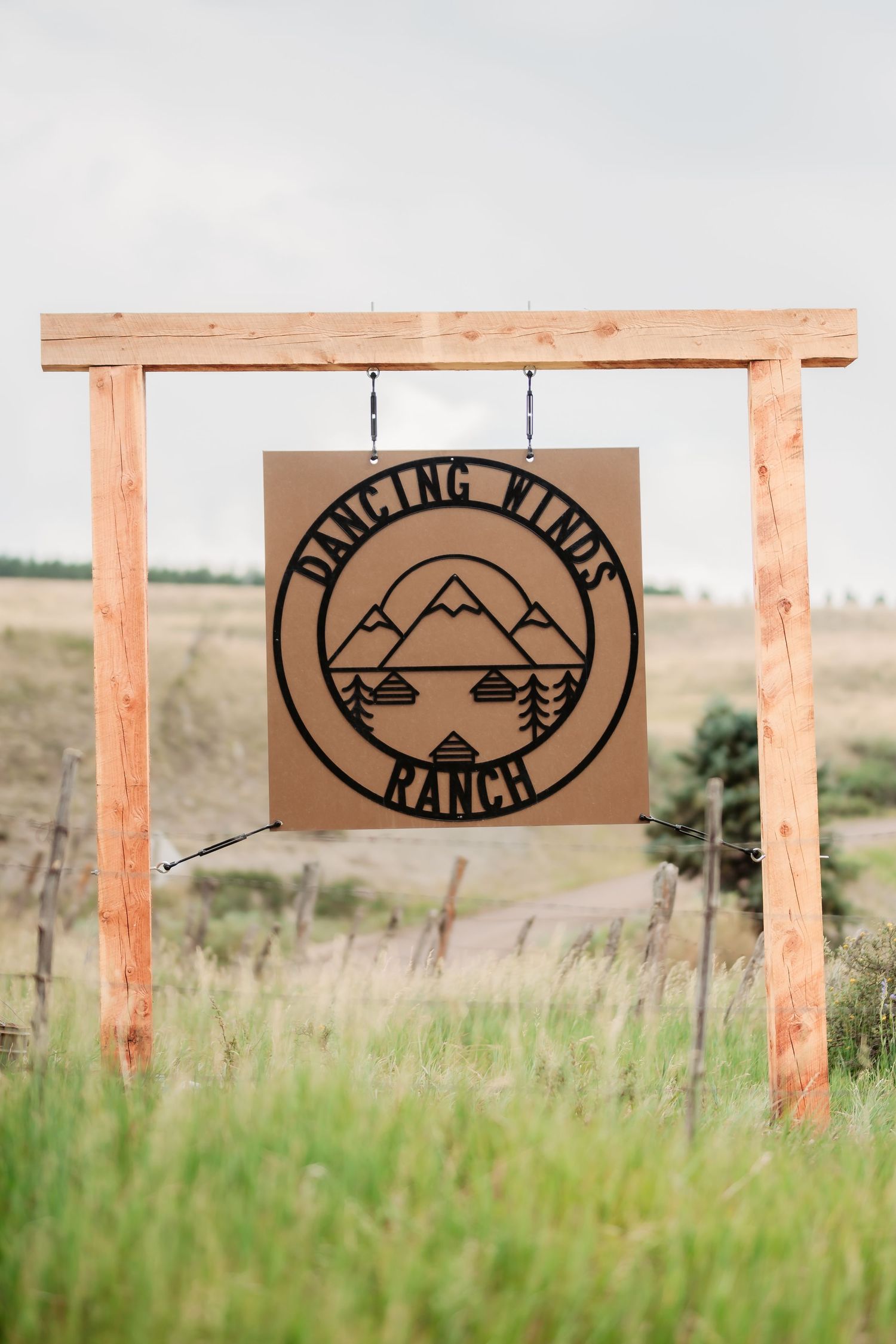 Rustic wooden ranch signs with mountain logos mounted on wooden posts in a grassy field.