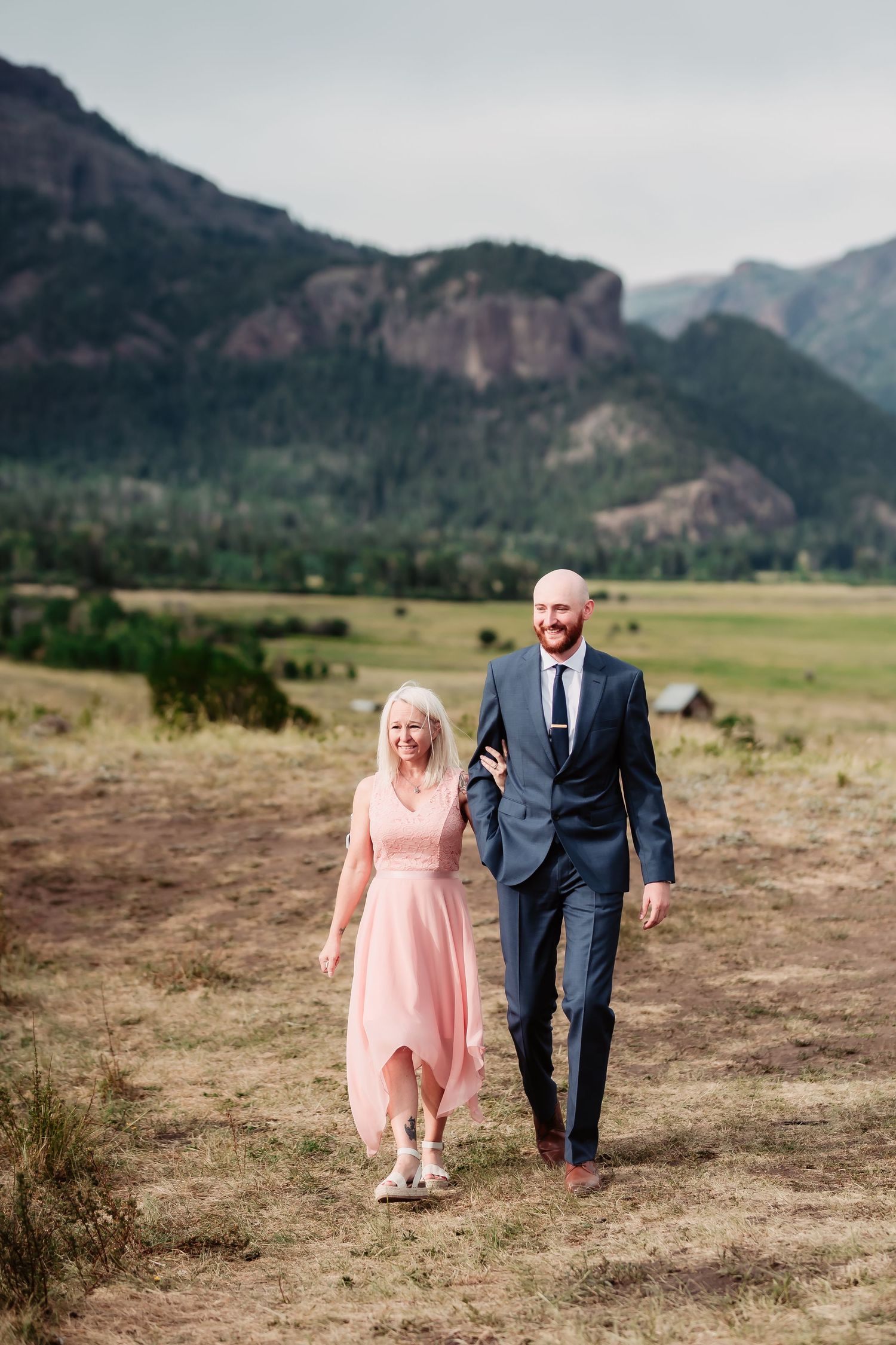A couple walks together in formal attire against a scenic mountain backdrop in Colorado.