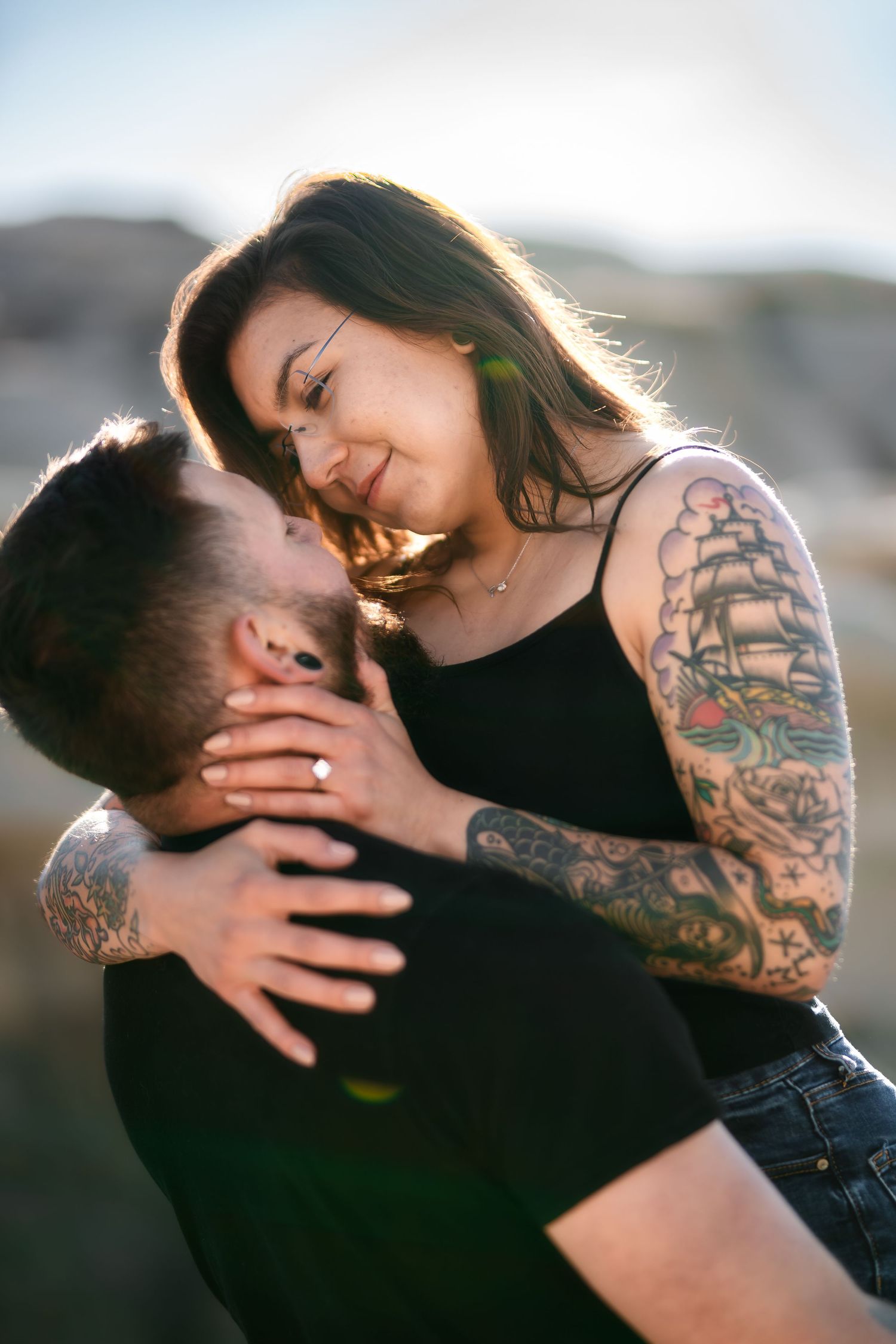 A romantic couple embraces intimately against a desert backdrop, with one person displaying artistic tattoos.