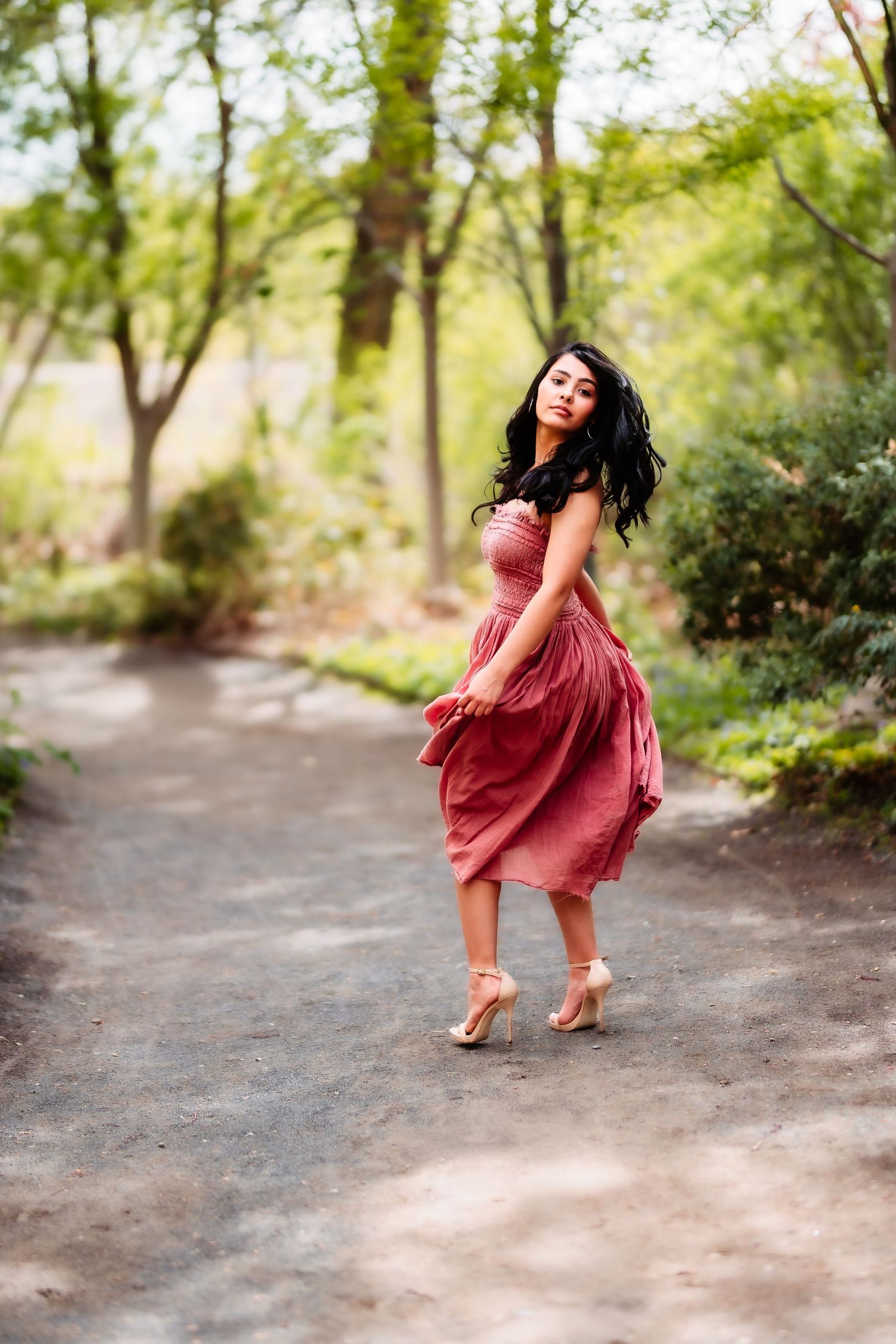 A twirling moment captured on a forest path showcases a flowing rose-colored dress.