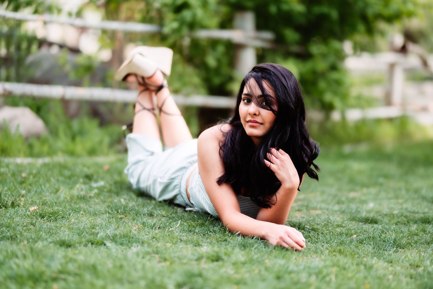 A woman with long dark hair relaxes while lying on green grass outdoors.