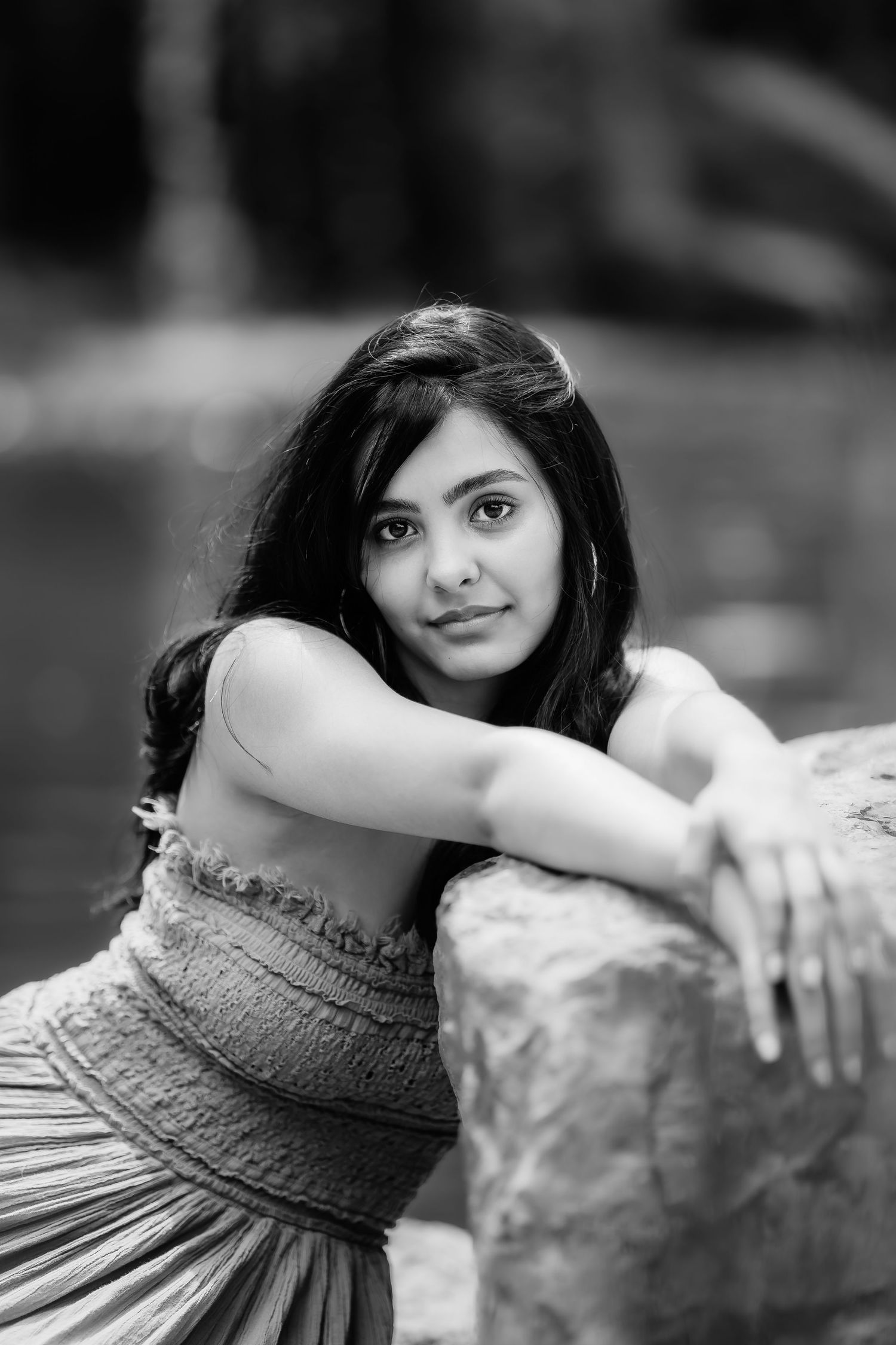 Black and white portrait showing artistic pose against stone wall in textured dress.