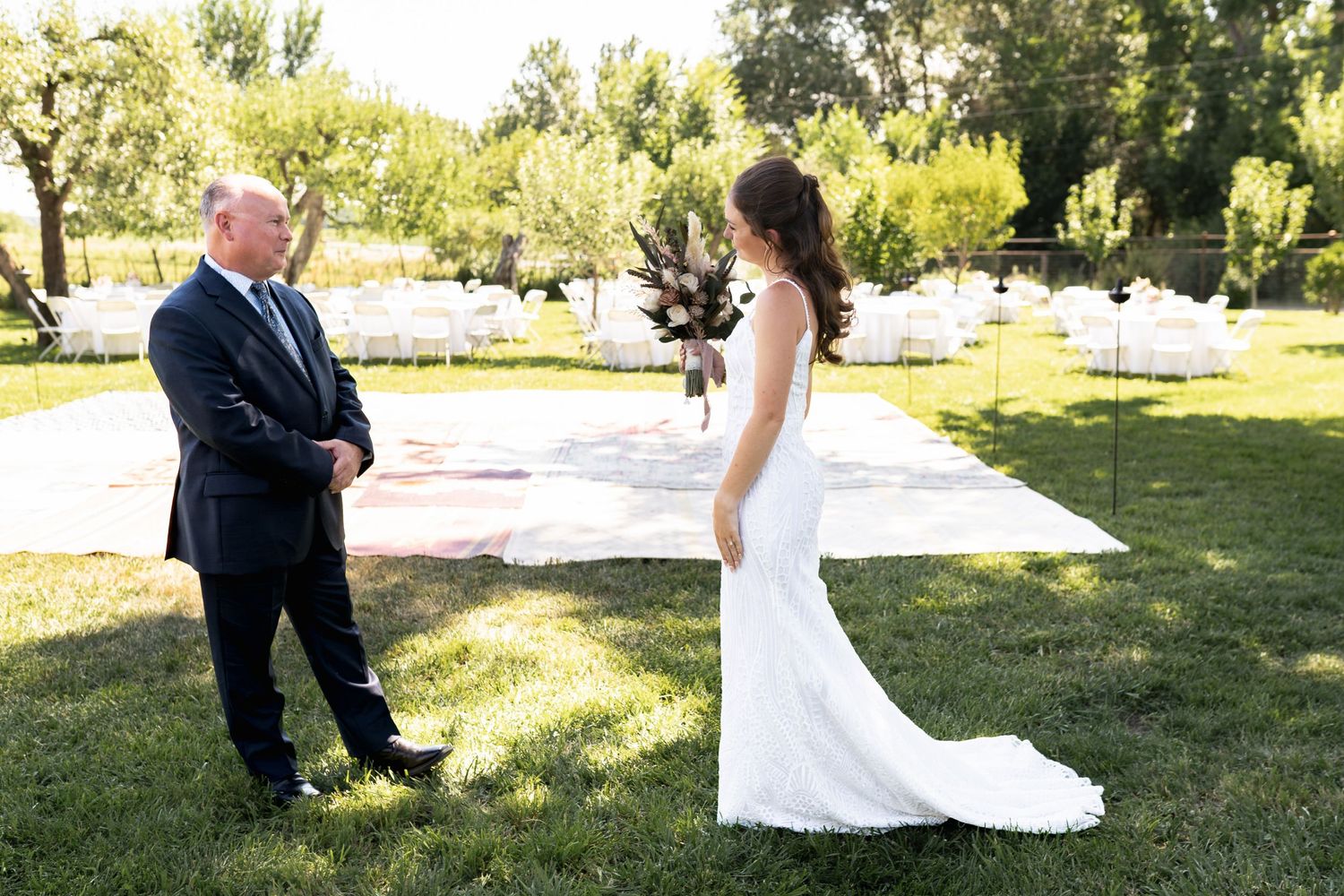 Two people share a moment outdoors on a sunny day in garden setting with green trees and grass.