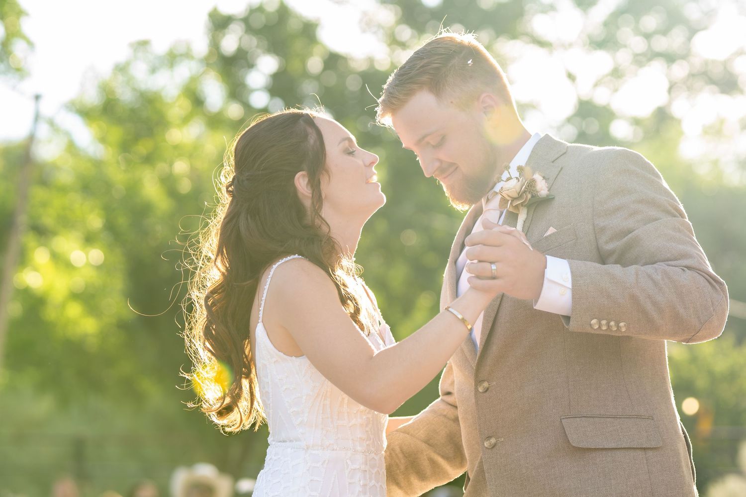 A couple shares their first dance together at a backlit outdoor wedding reception.