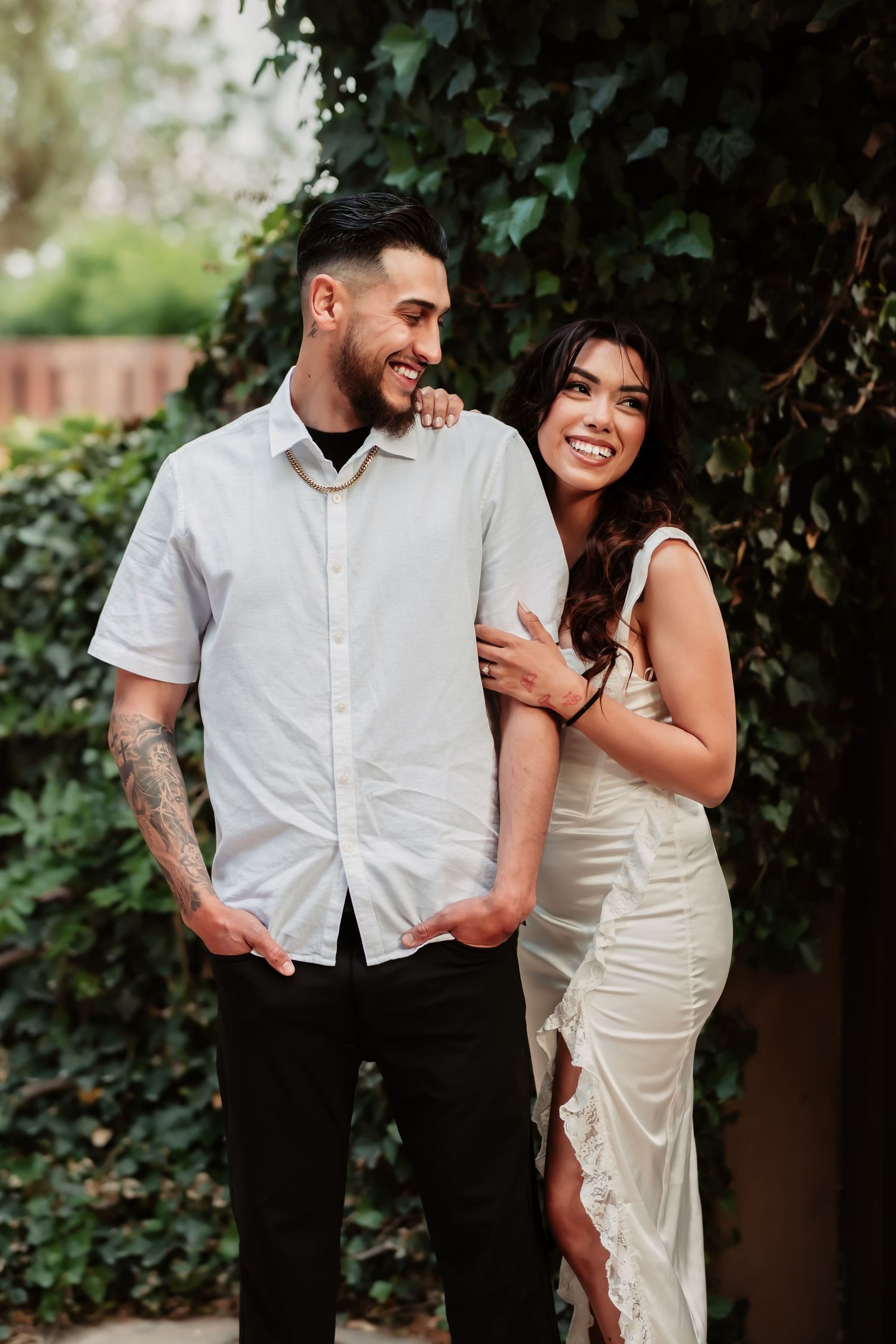 A romantic couple shares a tender moment against a backdrop of lush greenery and ivy-covered walls.