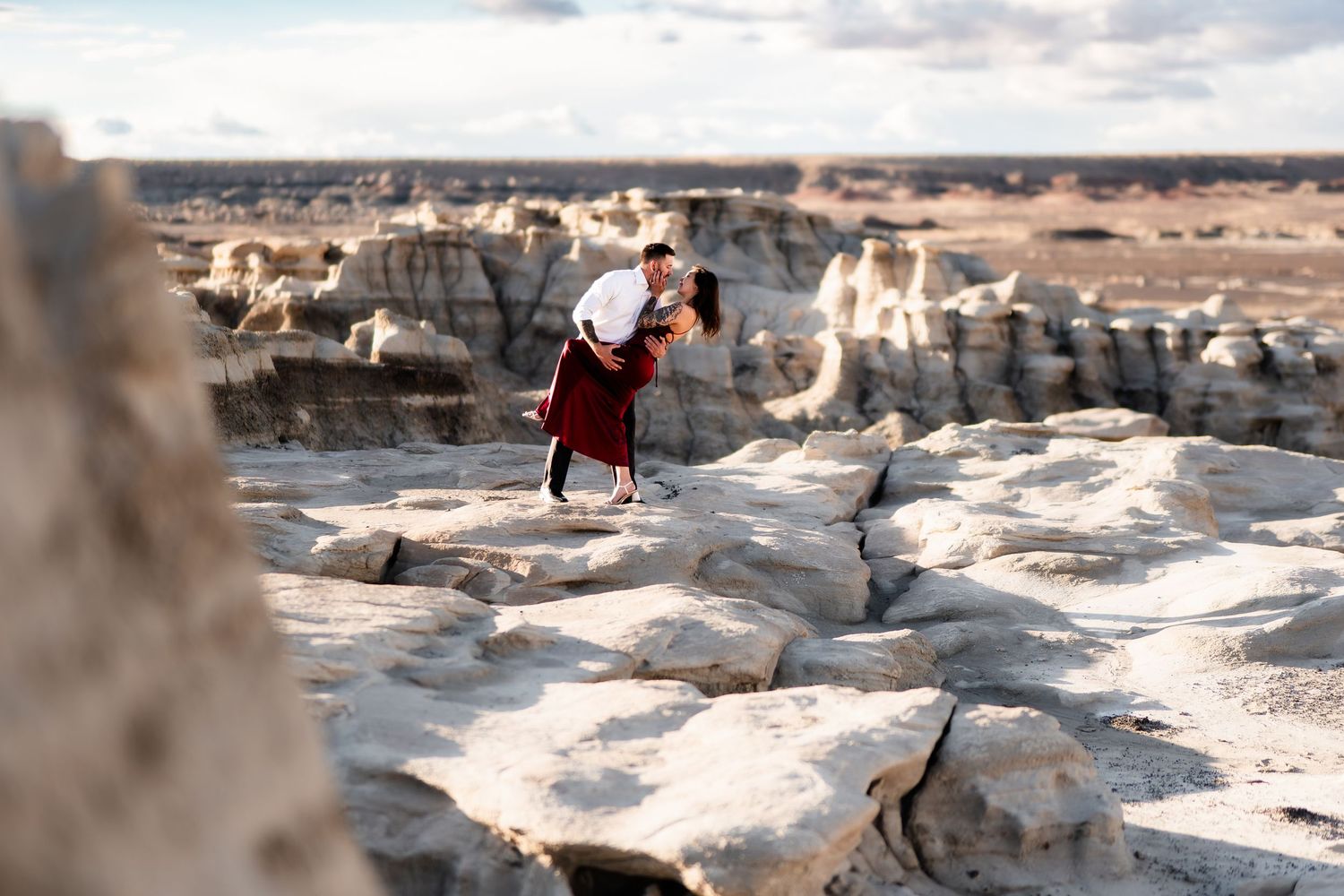 A person in red jumps across rugged white rock formations in a desert landscape.