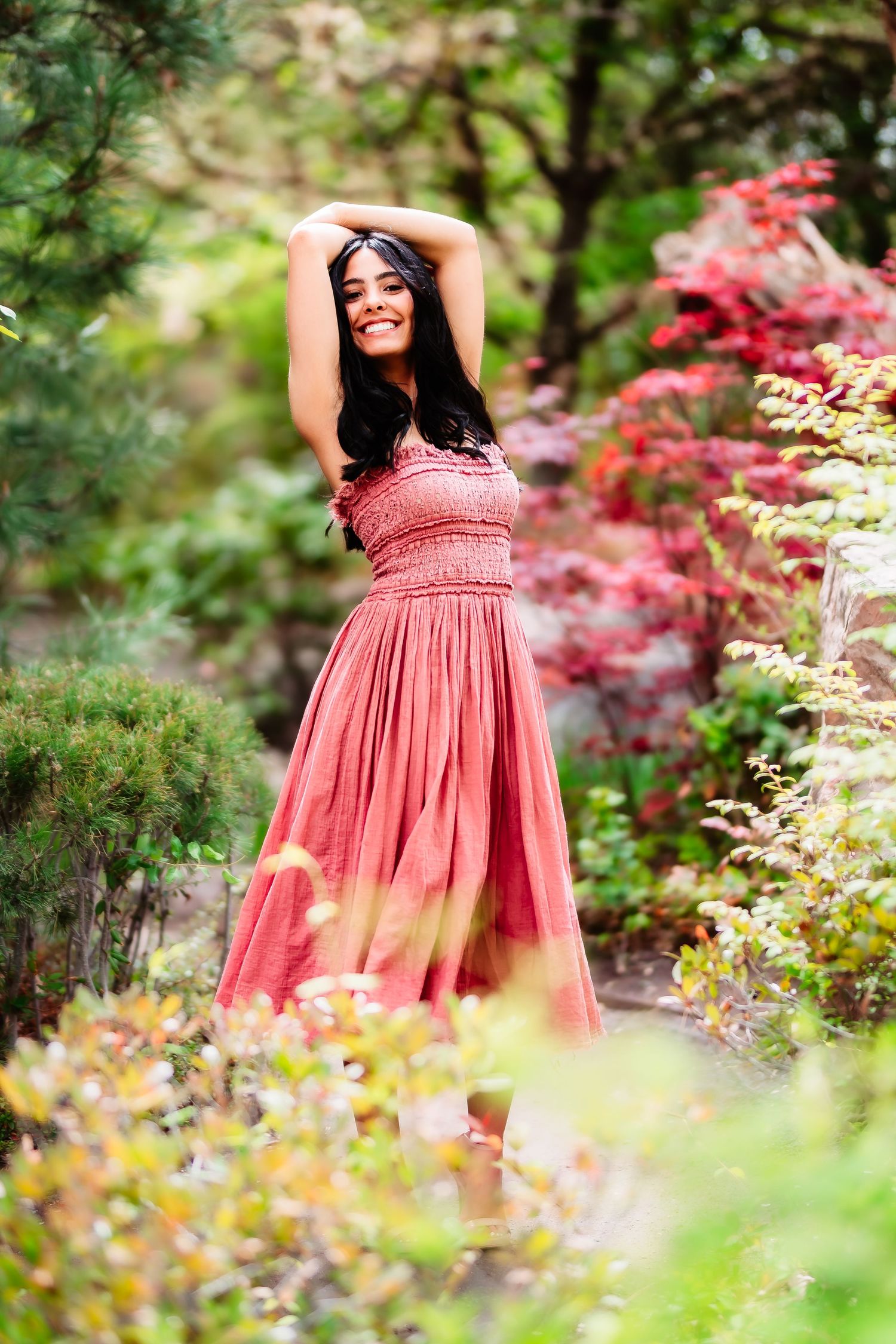 A flowing coral dress stands out against lush garden foliage and Japanese maple leaves.