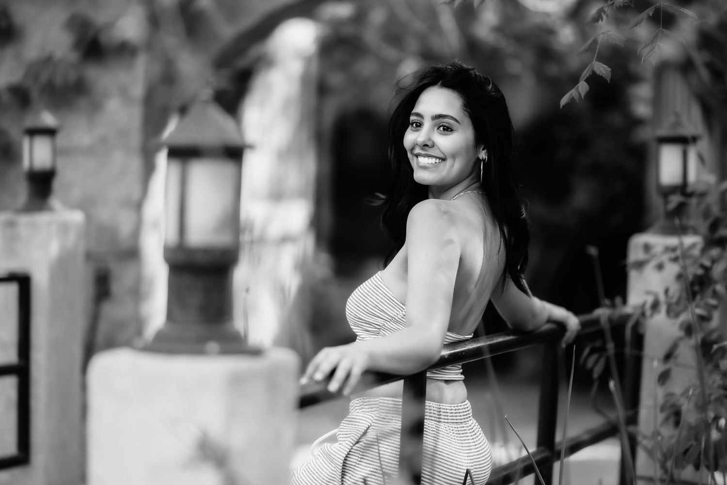 Black and white portrait capturing a natural smile while leaning against outdoor railing.