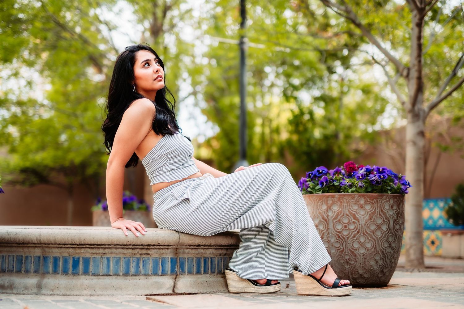 A casual outdoor portrait showing a woman in grey activewear relaxing on stone steps near a planted container.