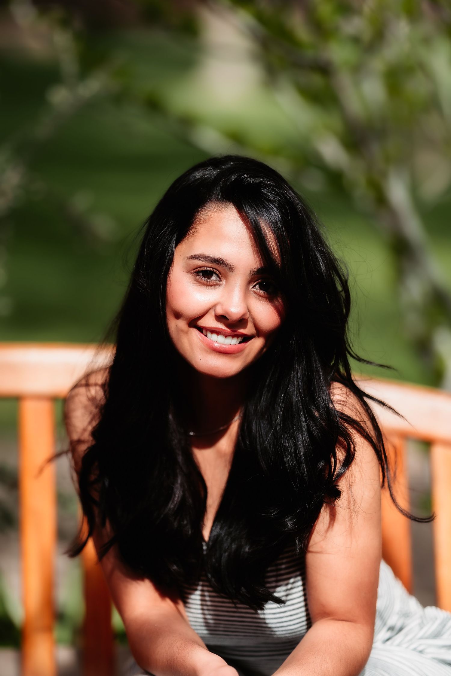 Close-up portrait featuring long dark hair and casual striped top against natural outdoor backdrop.