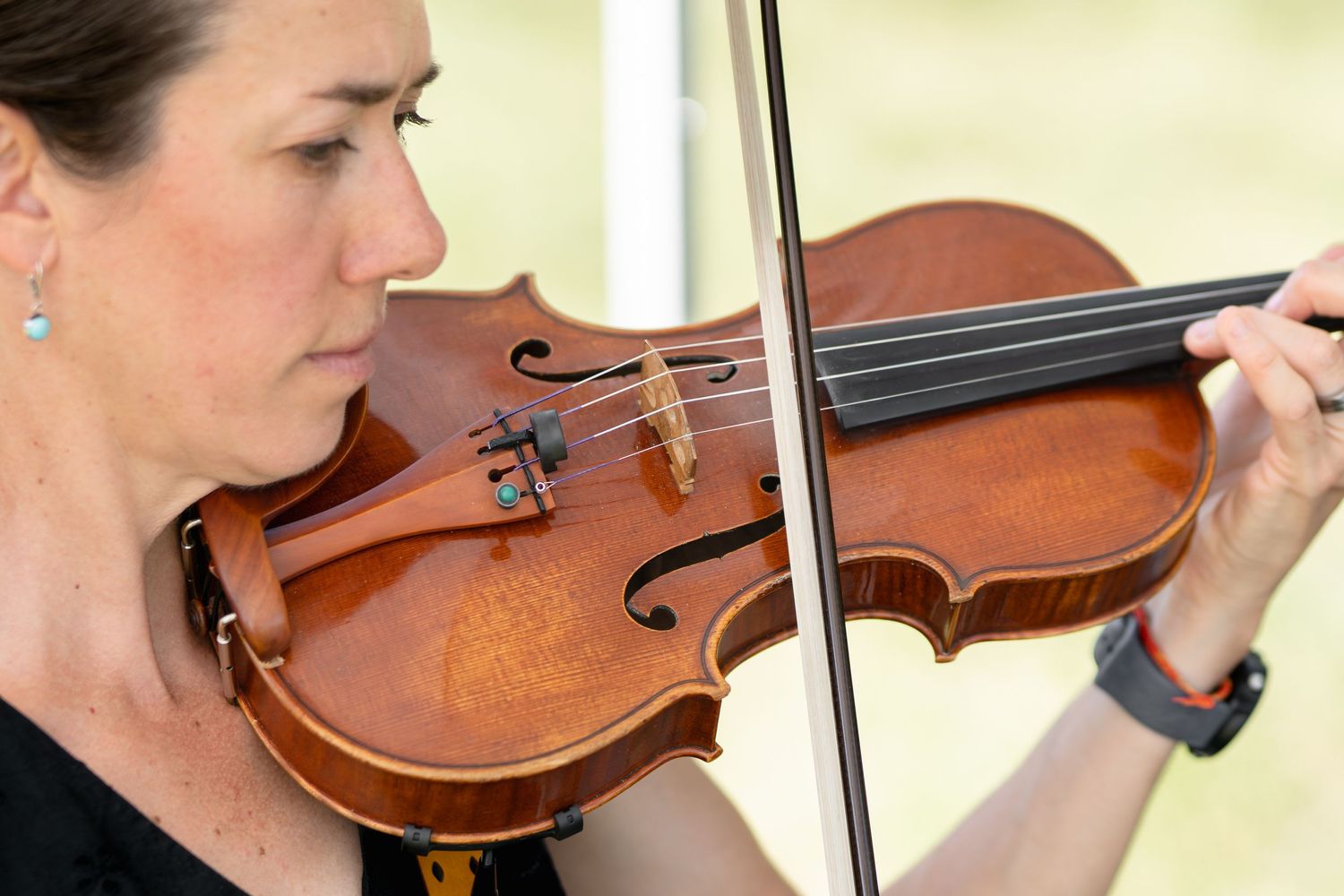 Close-up view of someone playing a rich brown violin with bow against a light background.
