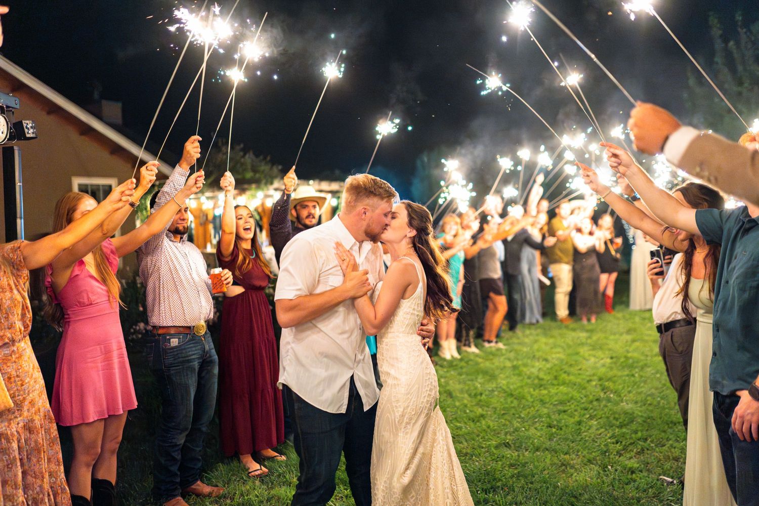 Wedding party and guests form a sparkler tunnel exit at an outdoor evening celebration.