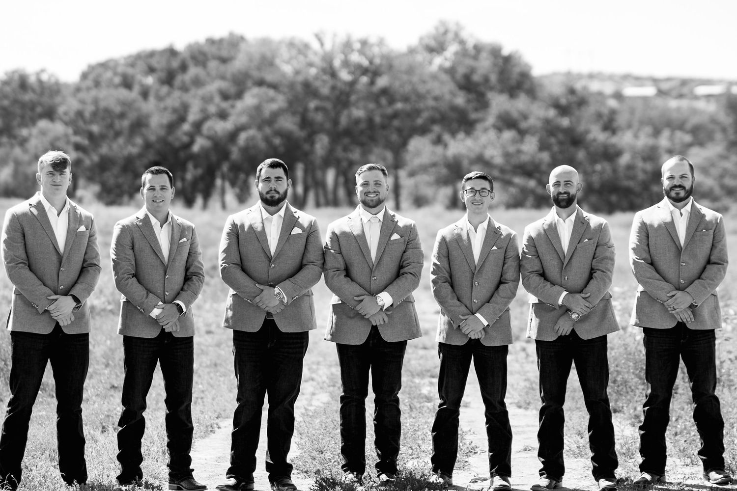 Seven groomsmen in matching gray suits lined up for formal black and white portrait.