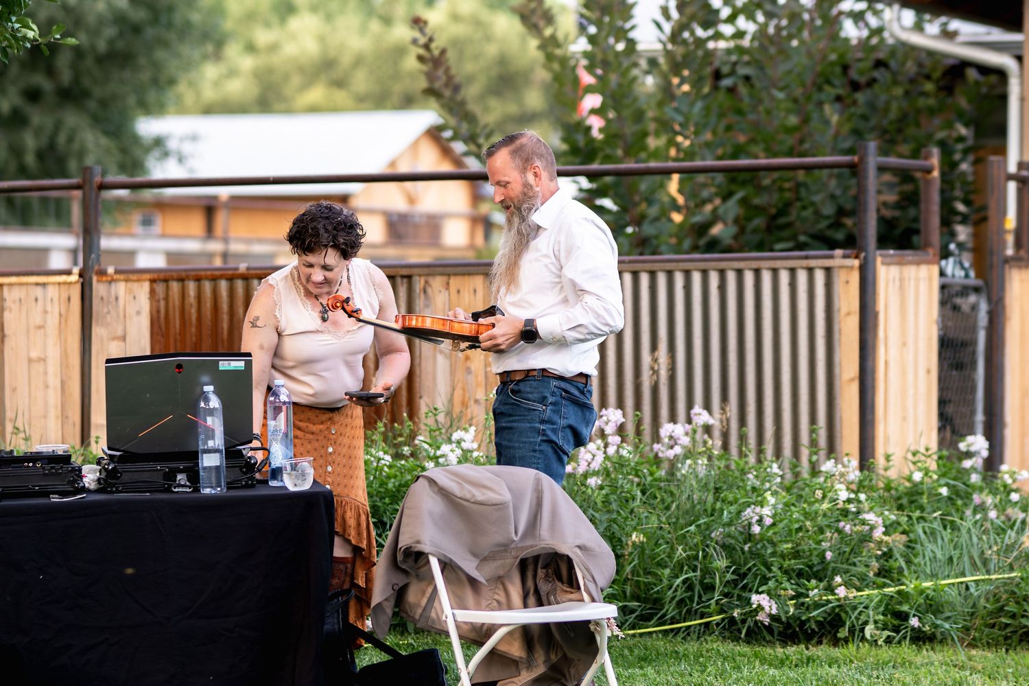 Musicians perform at an outdoor wedding reception with greenery and equipment setup.