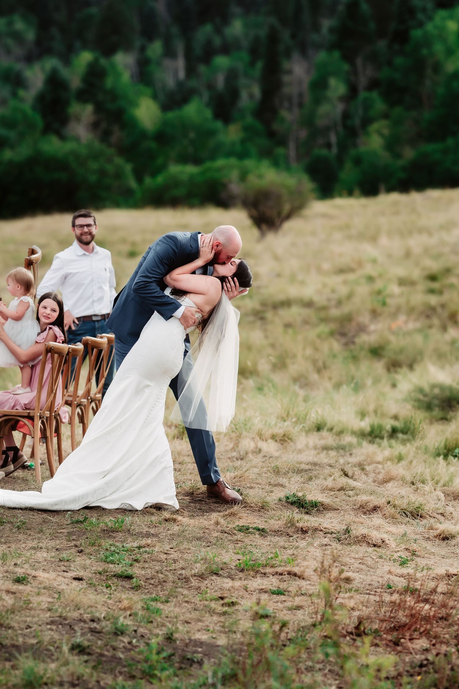 Wedding celebration with guests and couple on scenic mountainside meadow.