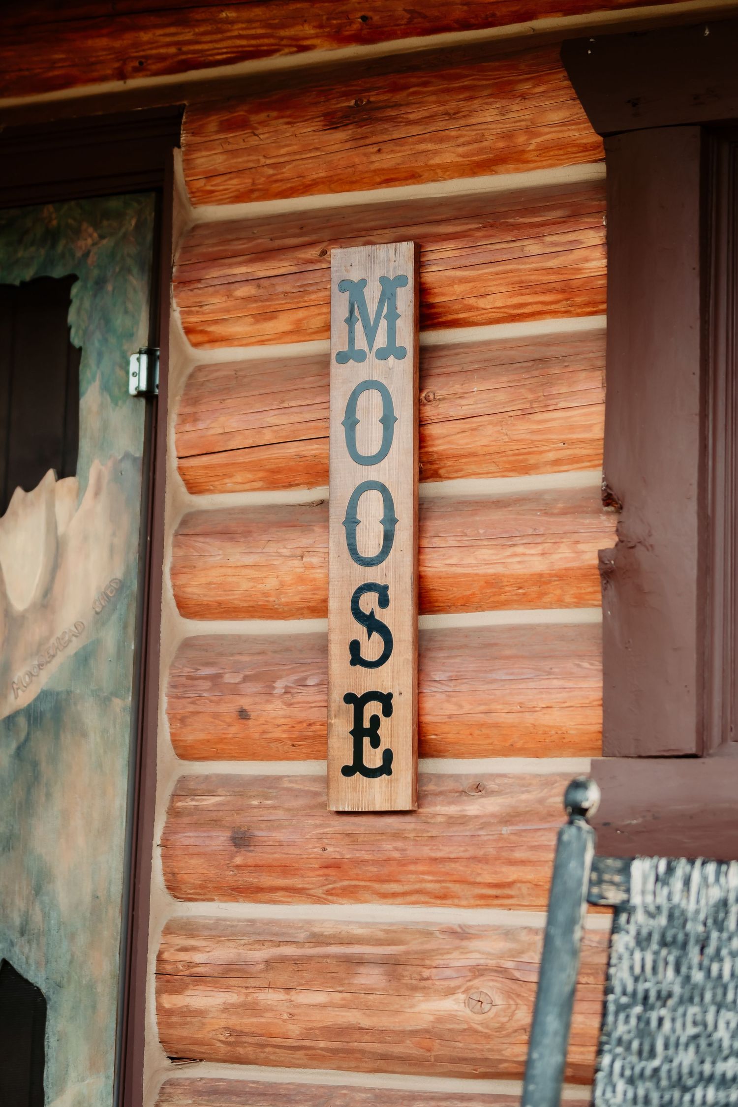 A rustic wooden log cabin wall displays a vertical blue 'MOOSE' sign.