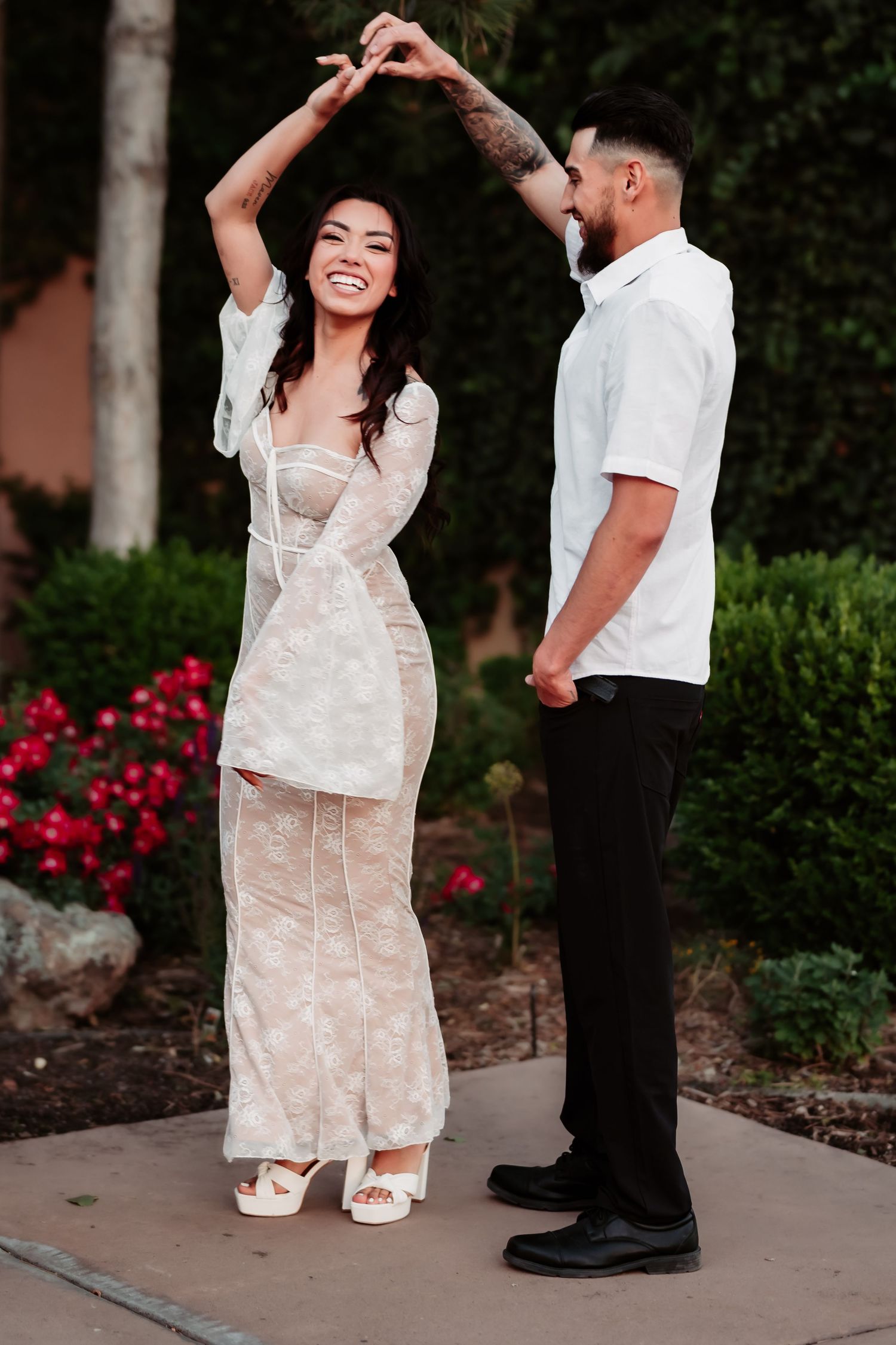 A joyful dancing moment outdoors with red flowers and greenery in the background.
