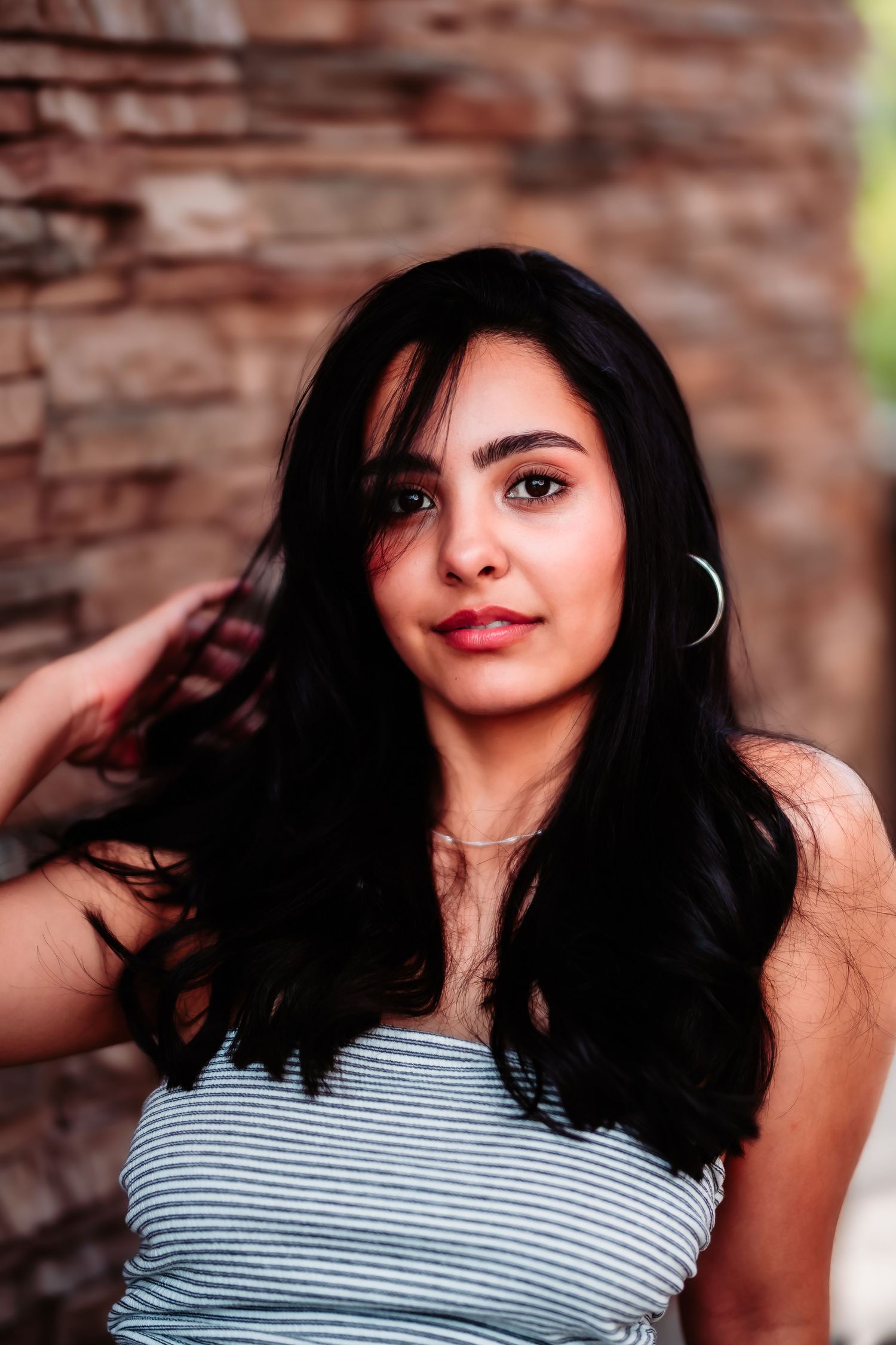 A woman in a striped top poses against a rustic brick wall background.